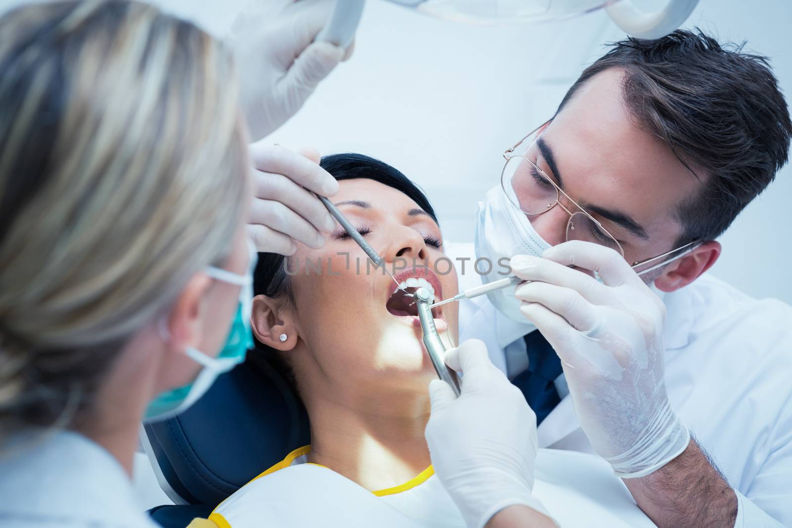 Male dentist with assistant examining womans teeth in the dentists chair