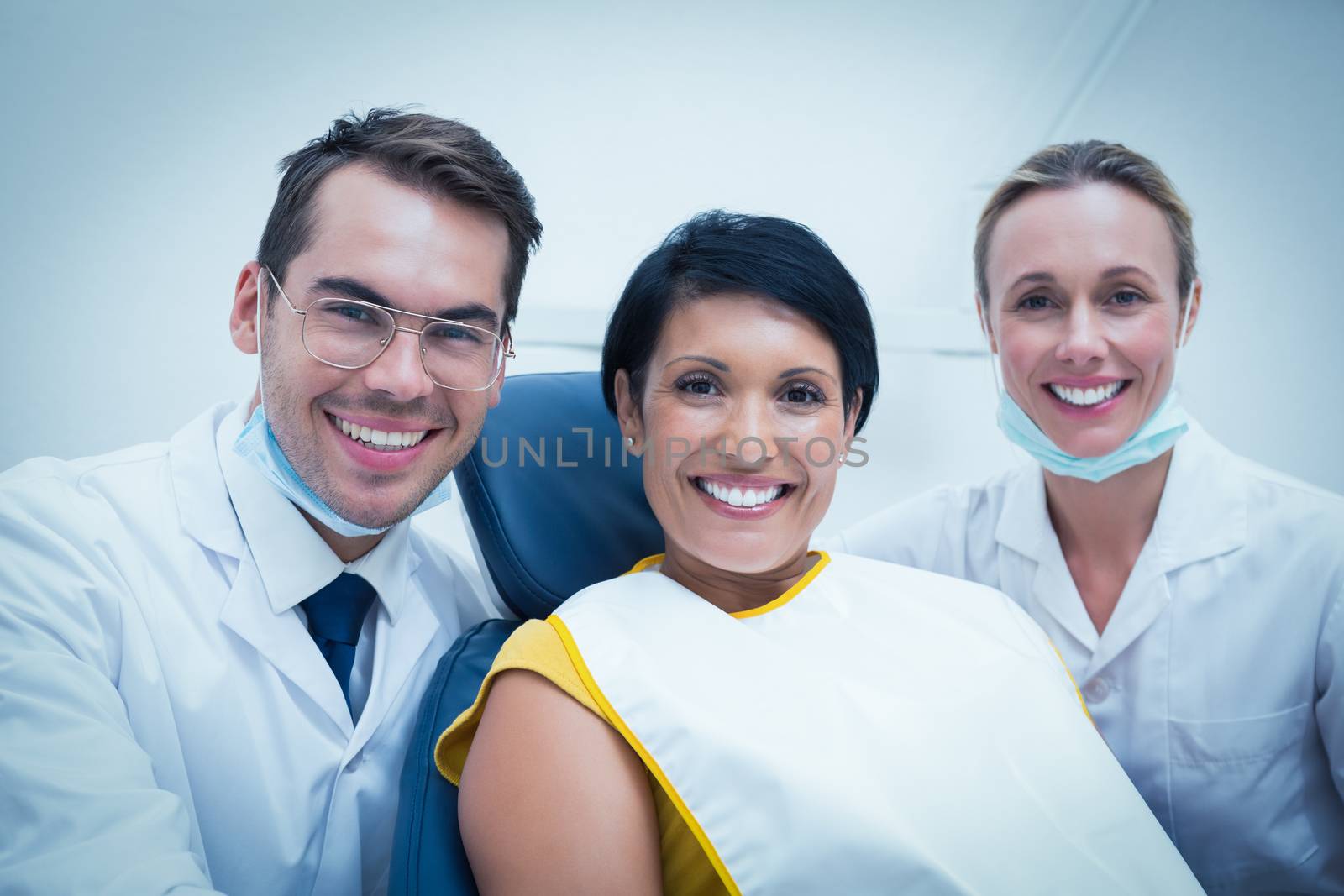 Portrait of smiling male dentist and assistant with female patient in the dentists chair