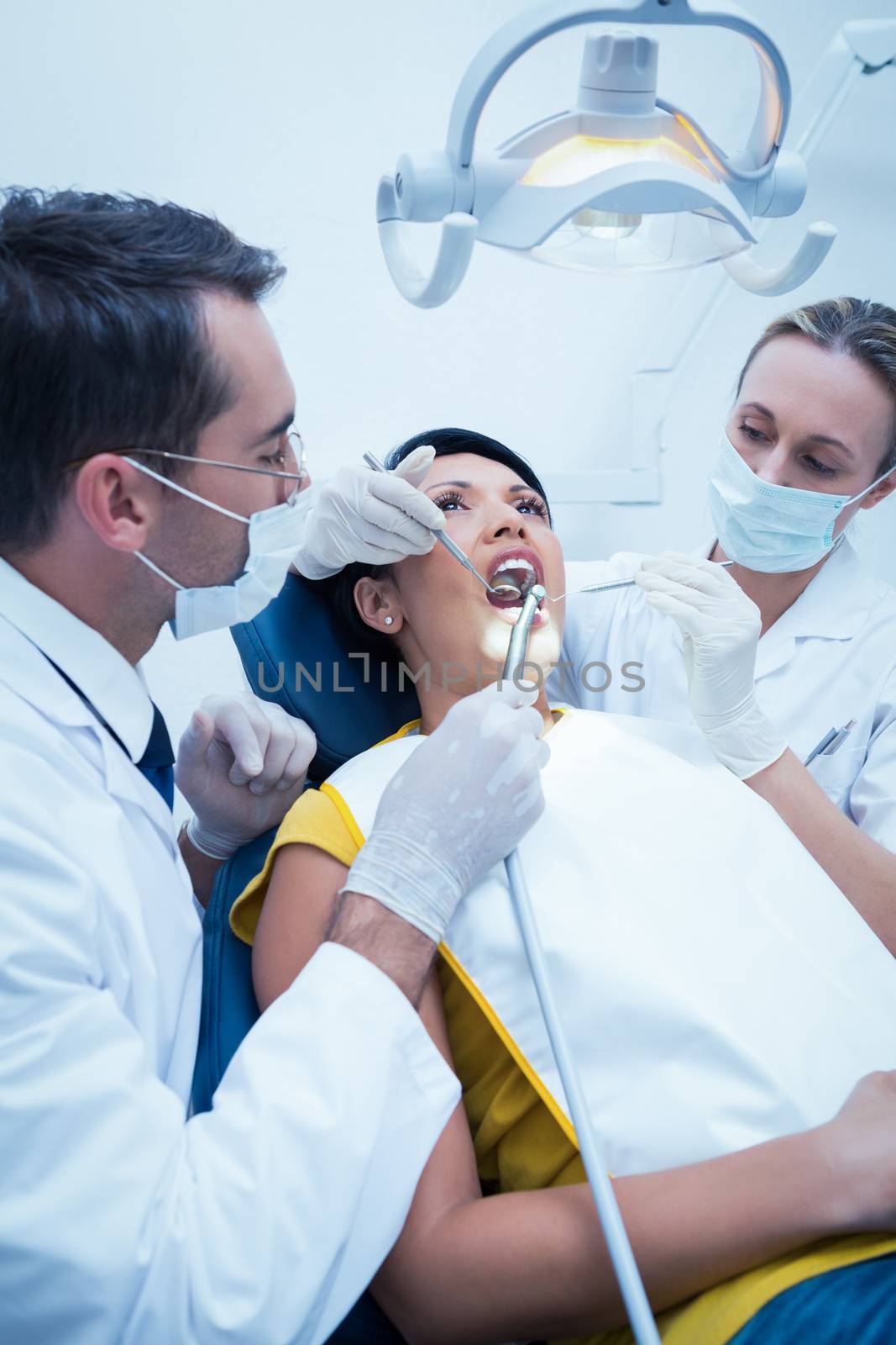 Male dentist with assistant examining womans teeth by Wavebreakmedia