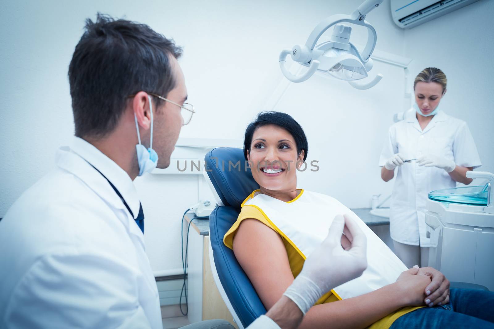 Male dentist and assistant with smiling female patient in the dentists chair