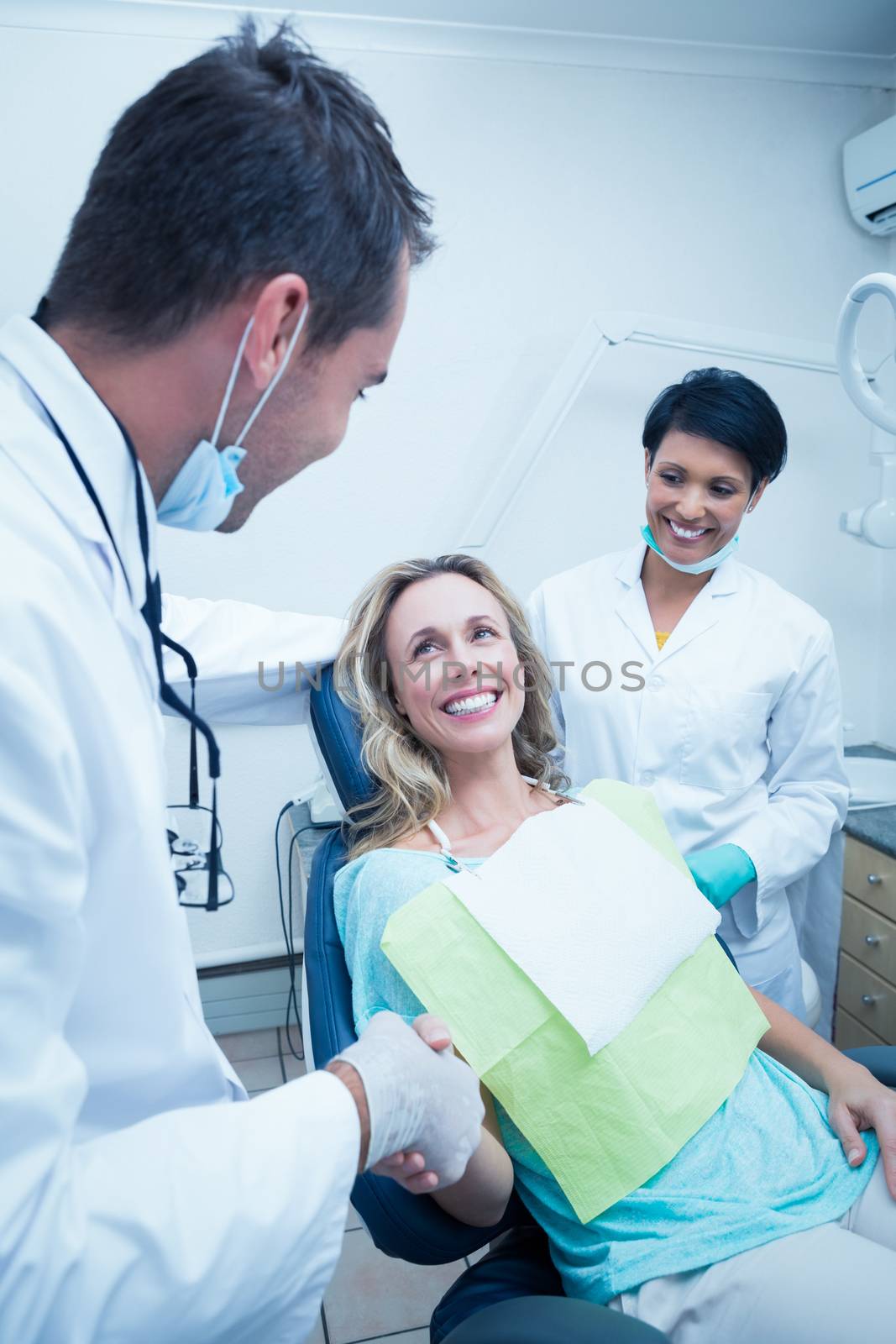Dentist with assistant shaking hands with woman by Wavebreakmedia