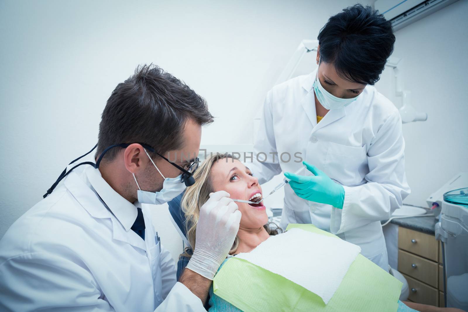 Male dentist with assistant examining womans teeth by Wavebreakmedia