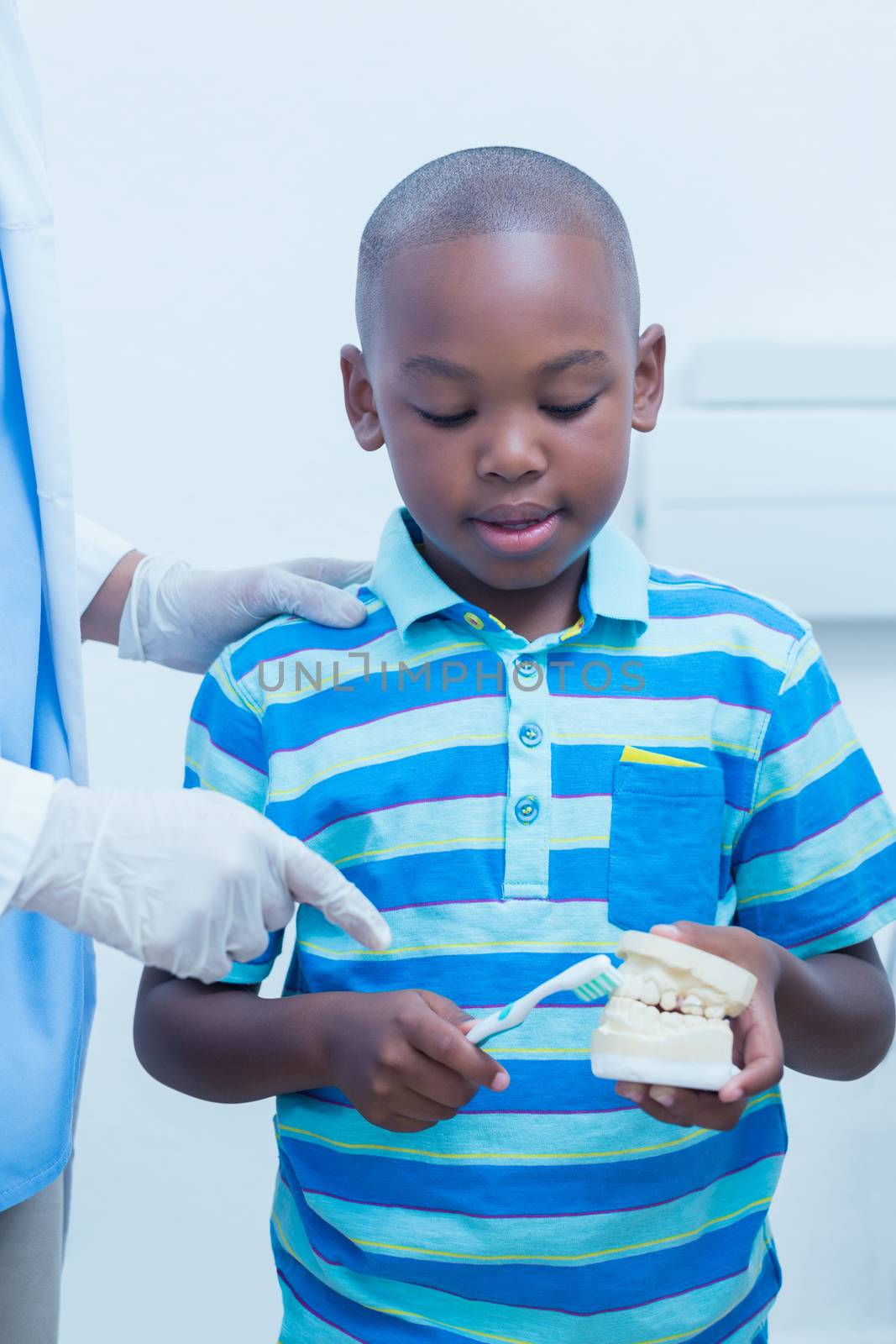 Dentist teaching boy how to brush teeth by Wavebreakmedia