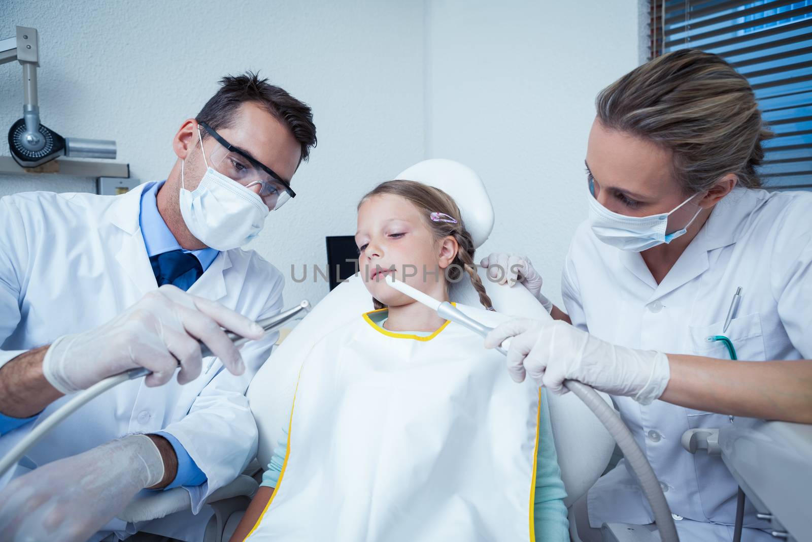 Dentist with assistant examining girls teeth in the dentists chair