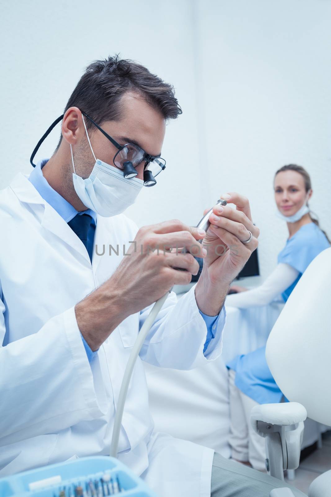 Concentrated young male dentist looking at dental tool