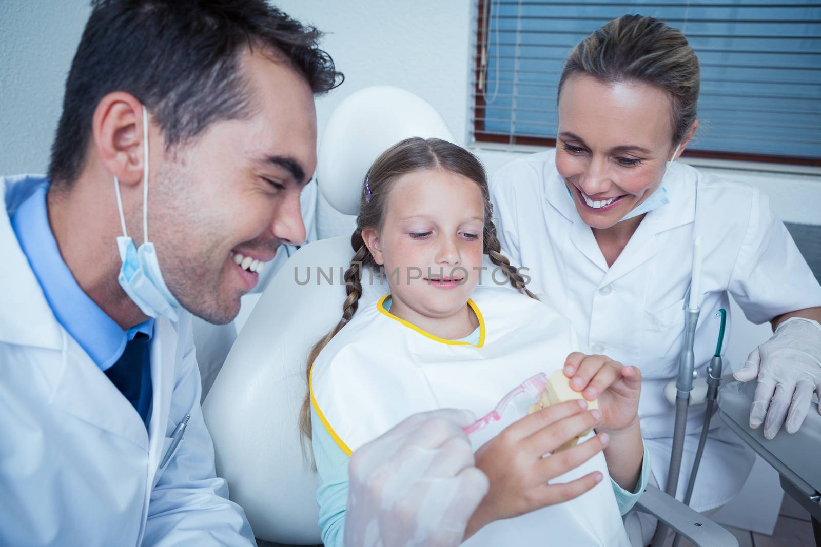 Dentist with assistant teaching girl how to brush teeth by Wavebreakmedia