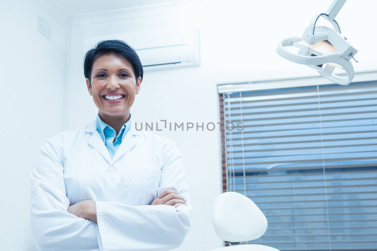 Portrait of smiling female dentist standing with arms crossed