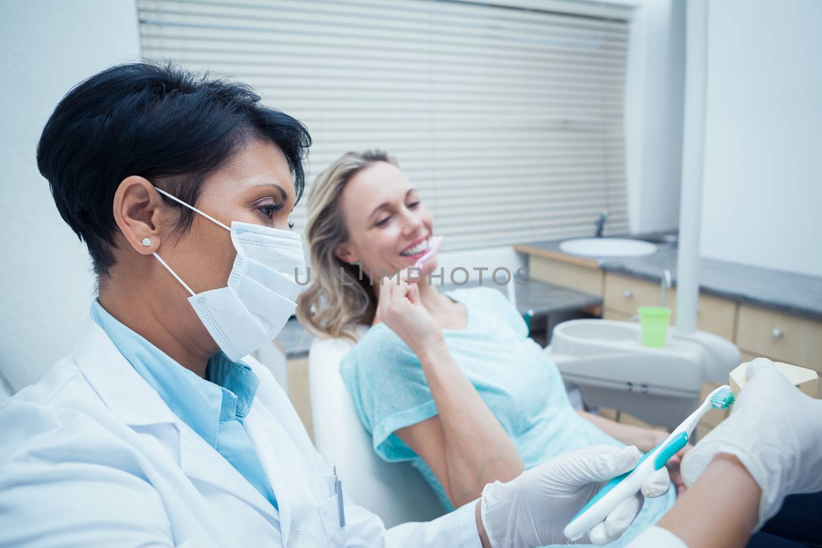 Female dentist showing woman how to brush teeth in the dentists chair