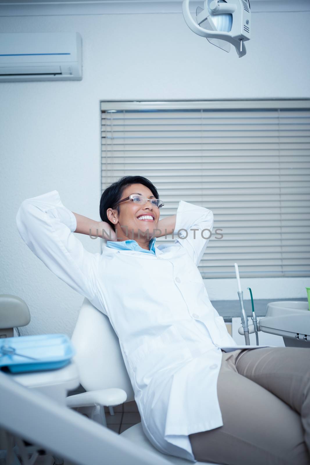 Relaxed smiling female dentist sitting on chair with hands behind head