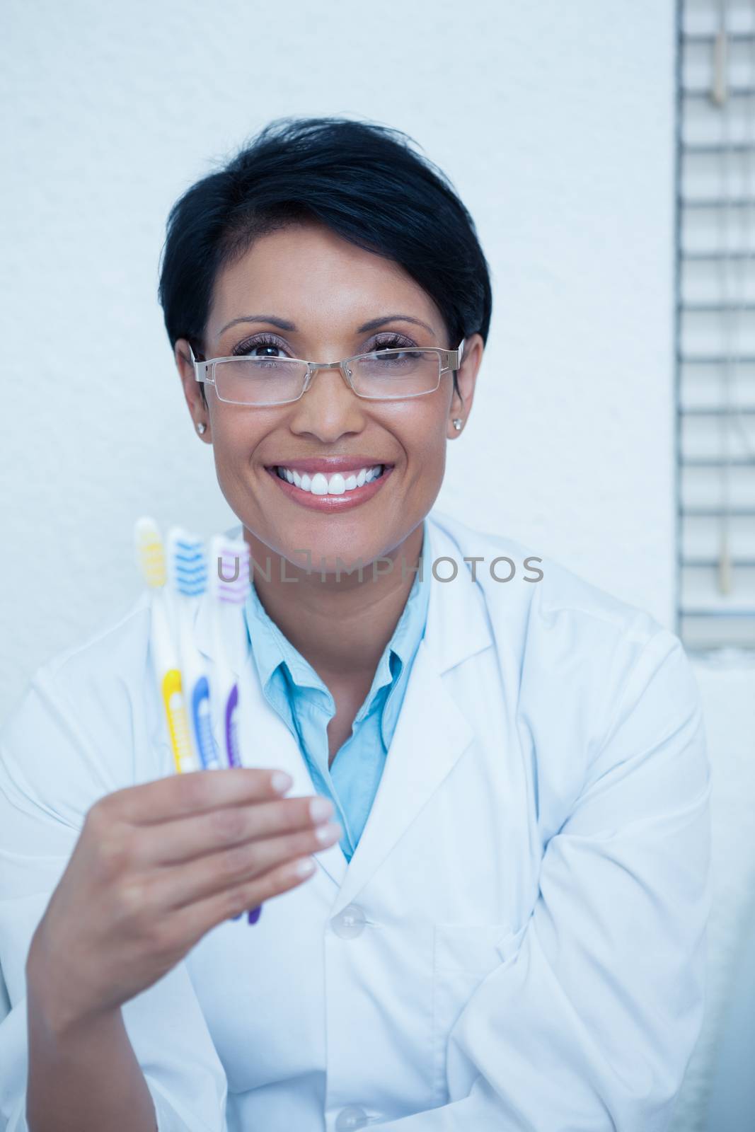 Portrait of smiling young female dentist holding toothbrushes