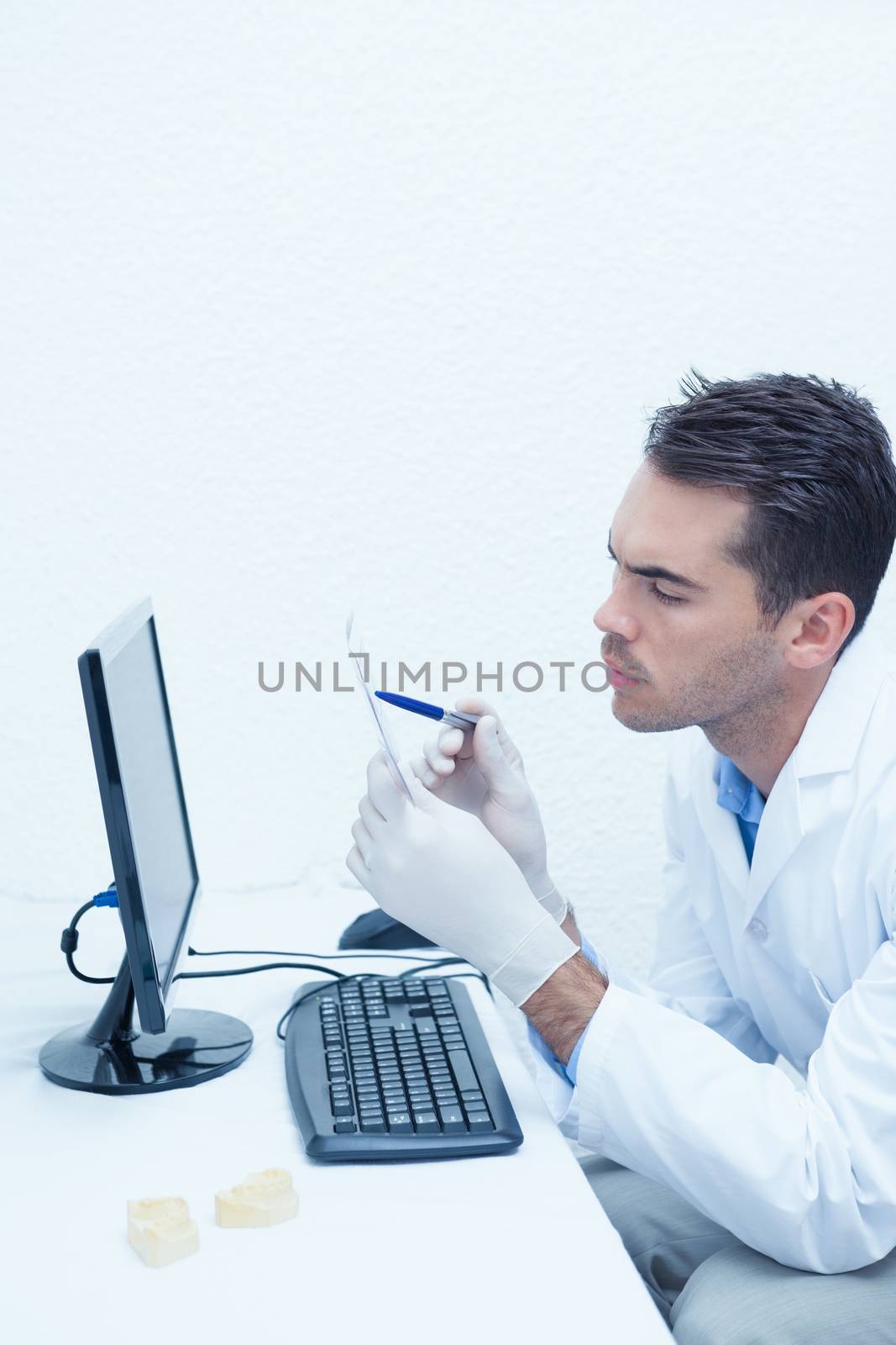 Concentrated male dentist looking at x-ray by computer