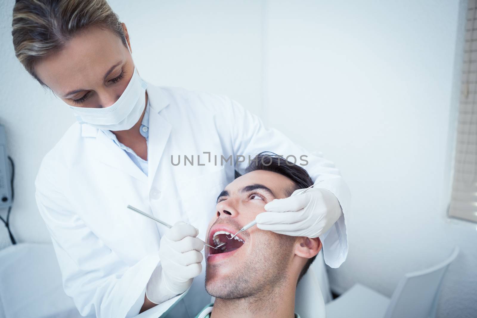 Female dentist examining mans teeth by Wavebreakmedia