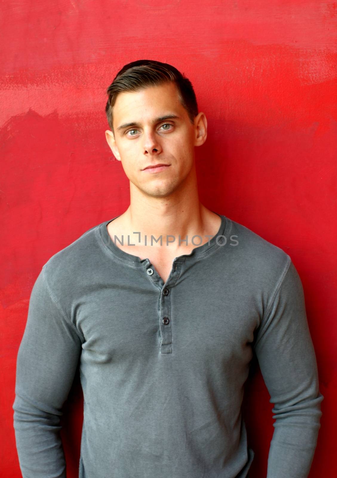 Portrait of a man standing in front of a red wall.