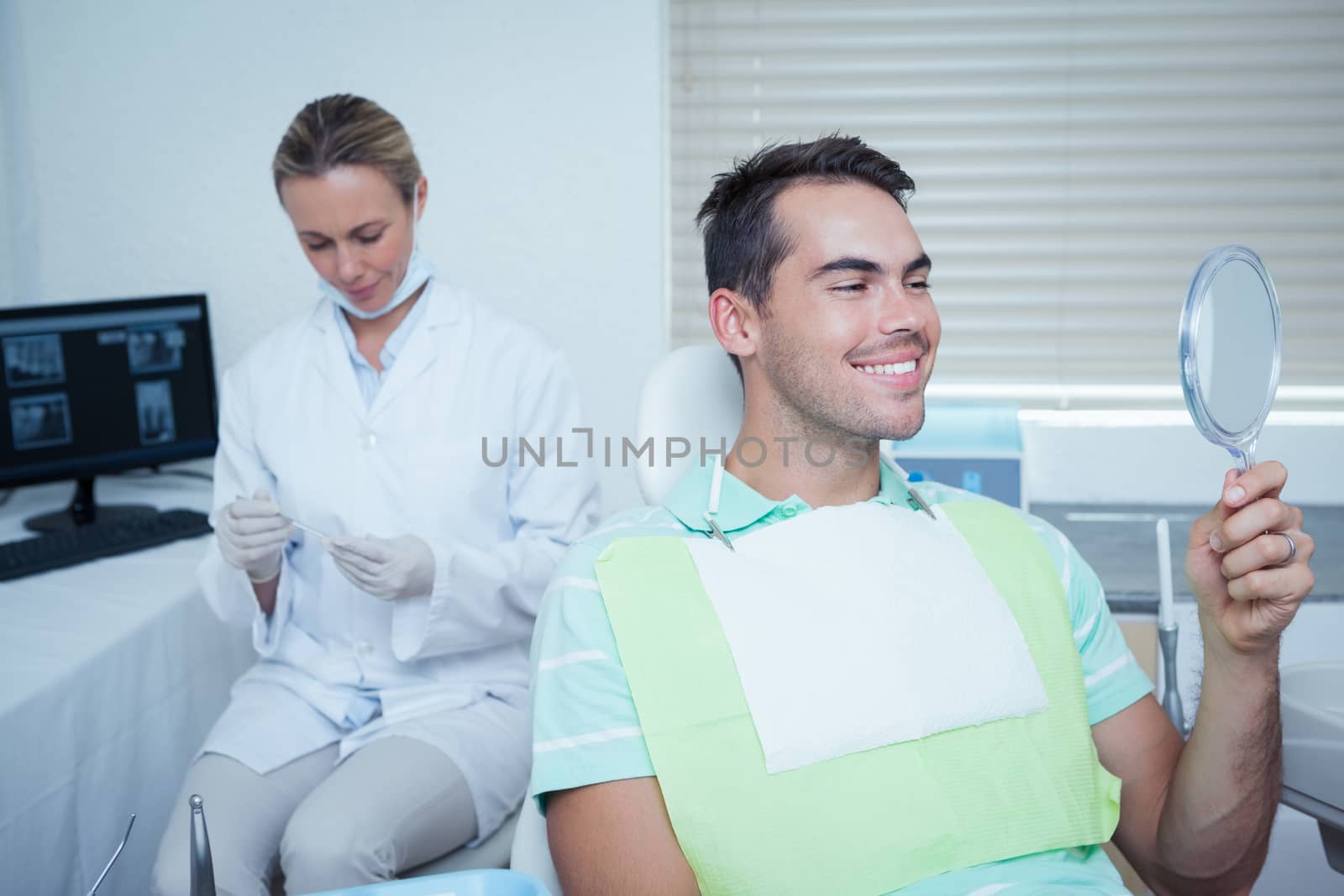 Smiling young man looking at mirror in the dentists chair