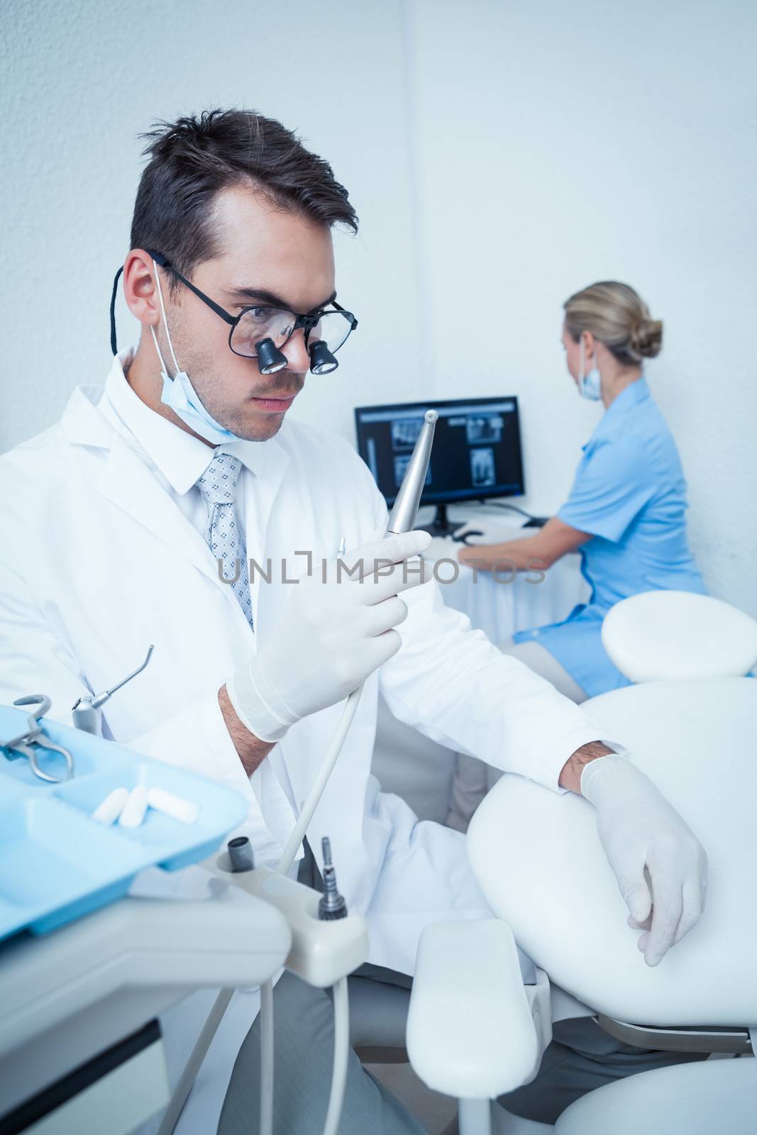 Concentrated male dentist looking at dental drill