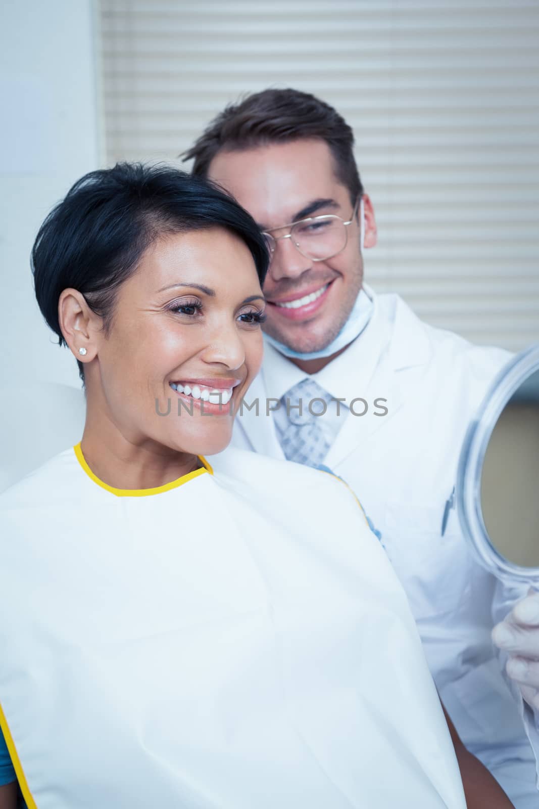 Smiling young woman looking at mirror in the dentists chair