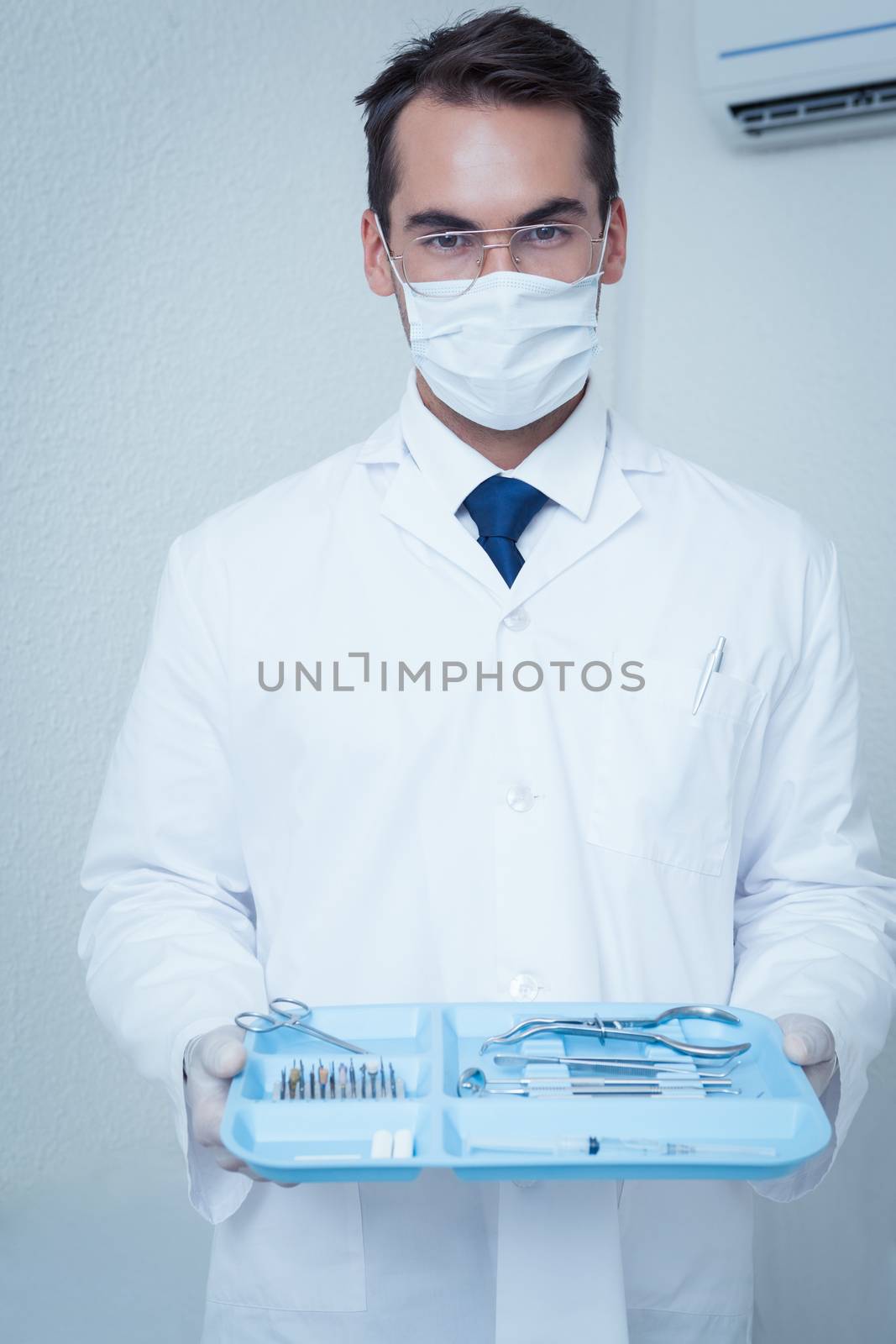 Portrait of male dentist in surgical mask holding tray of tools