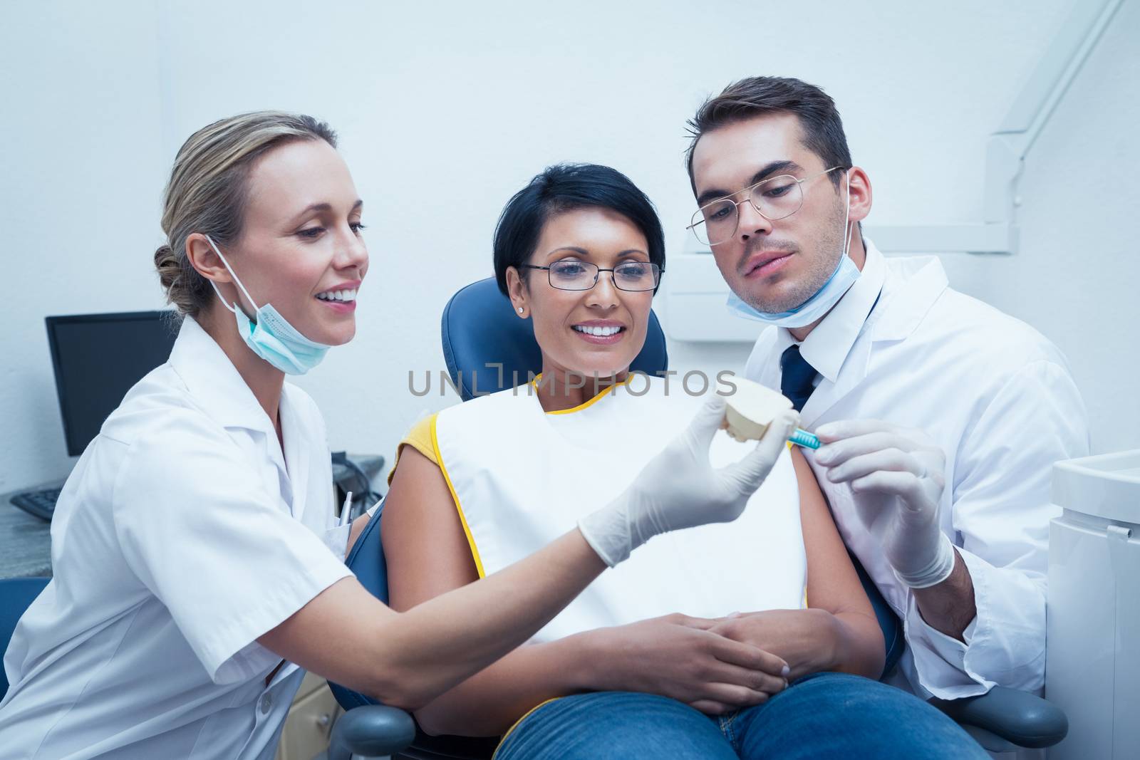 Female dentist with assistant showing woman prosthesis teeth