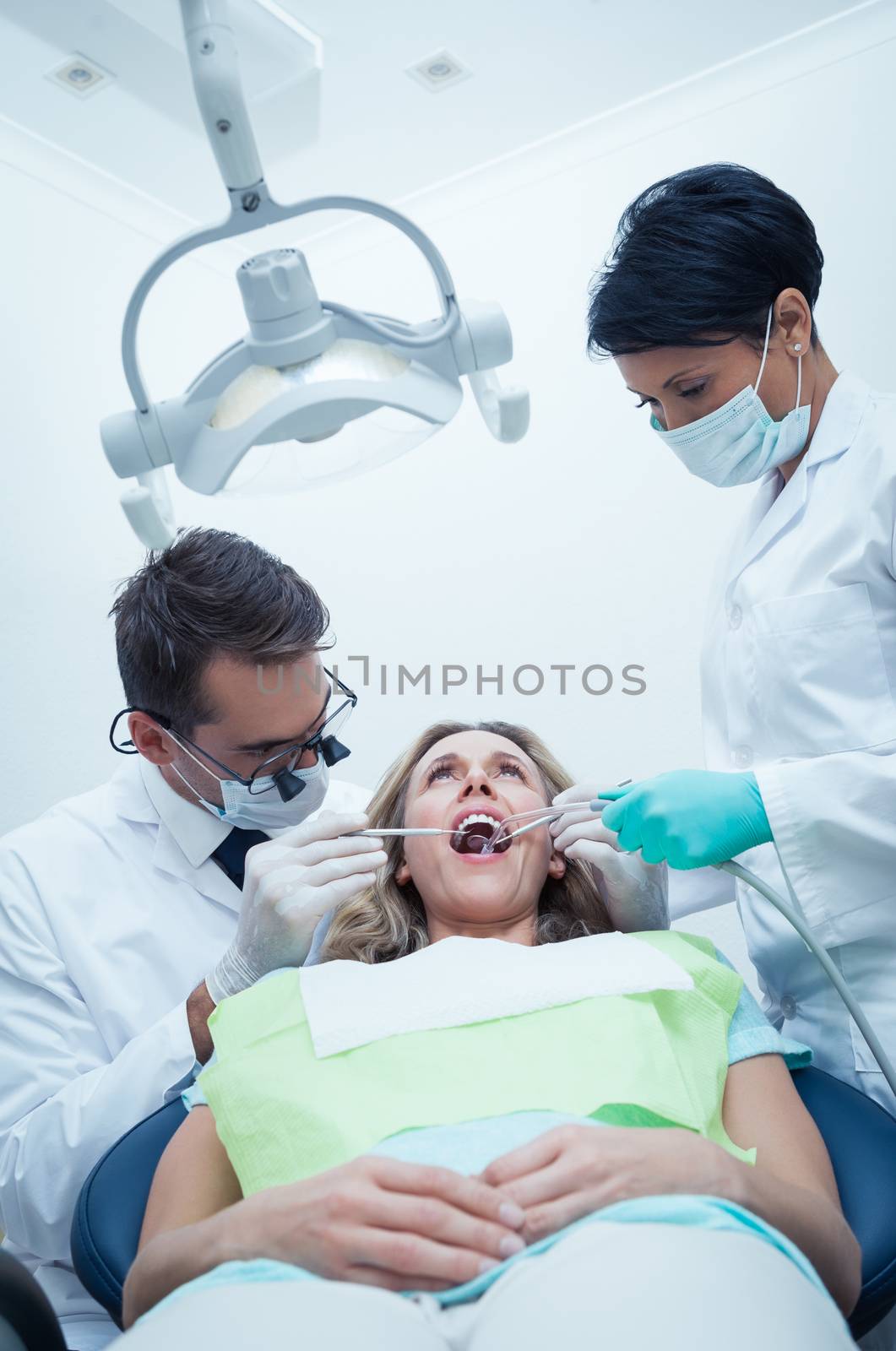 Dentist with assistant examining womans teeth by Wavebreakmedia