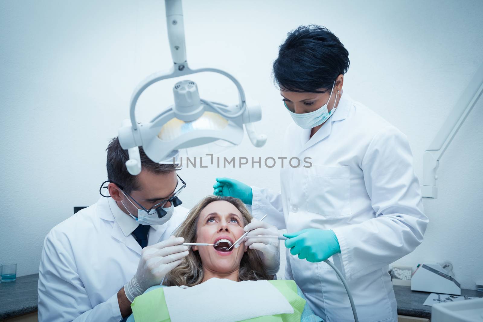 Dentist with assistant examining womans teeth by Wavebreakmedia