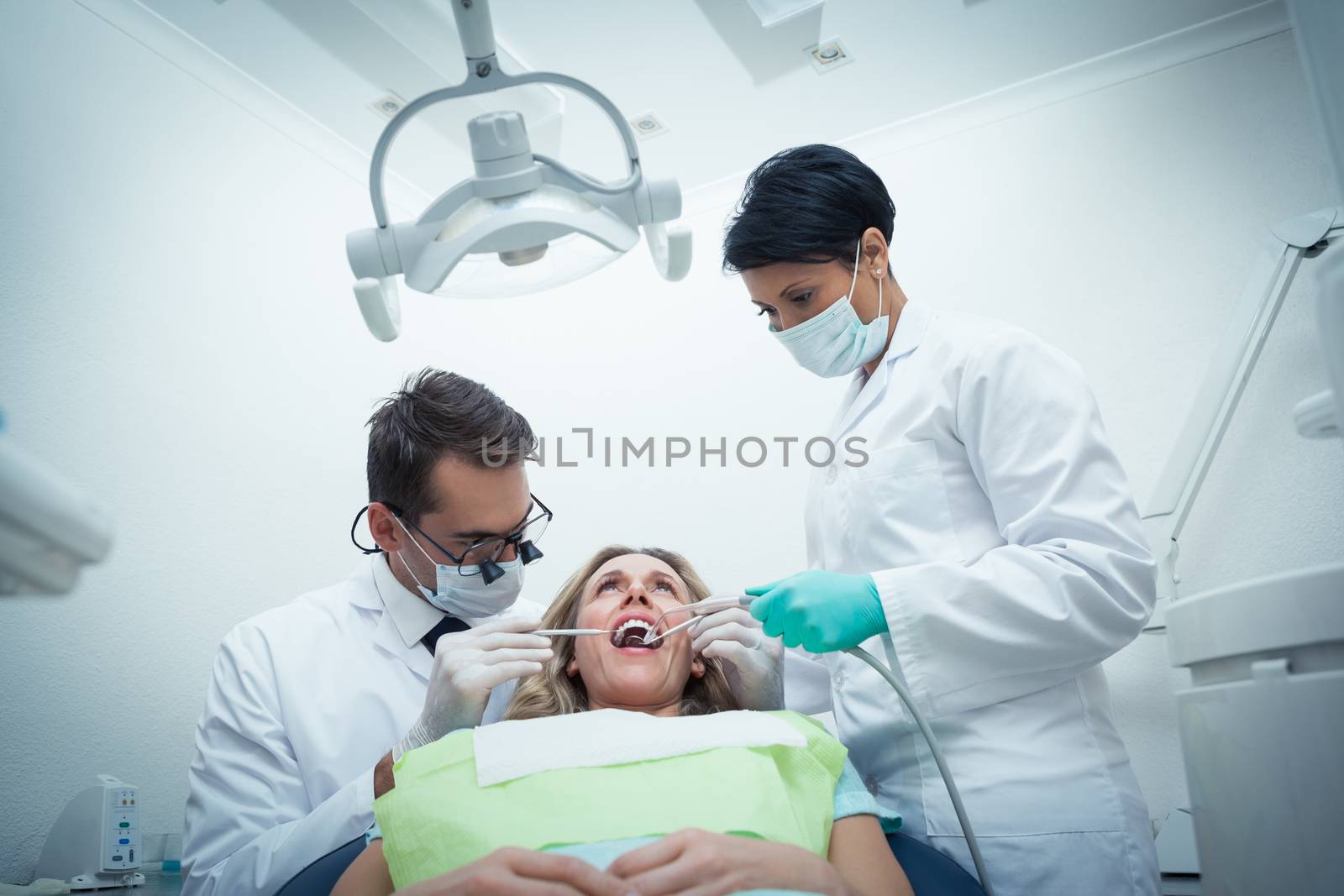 Male dentist with assistant examining womans teeth in the dentists chair