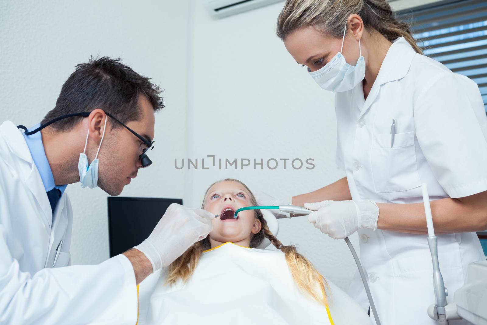 Dentist  with assistant examining girls teeth by Wavebreakmedia