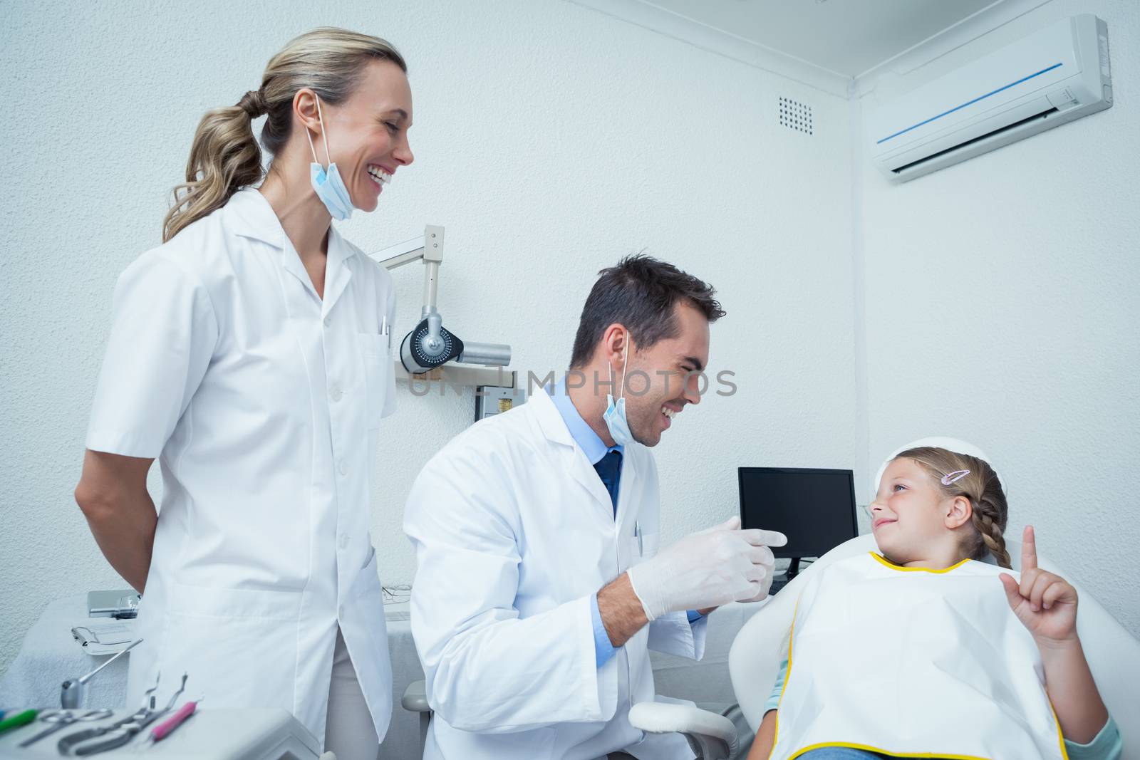 Male dentist  and assistant talking to girl in the dentists chair