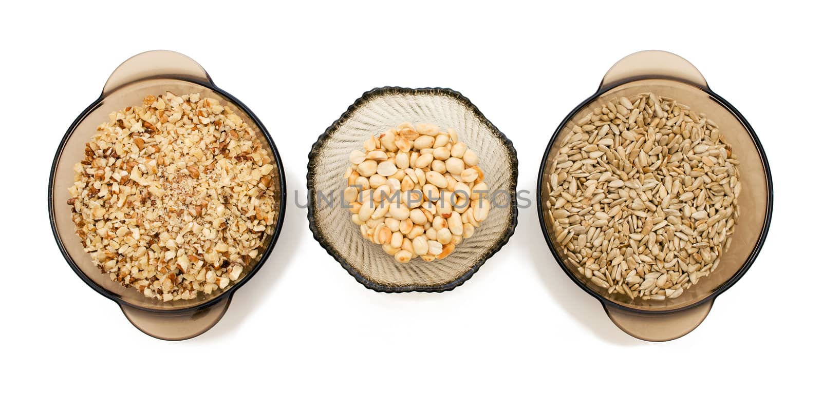 Food ingredients: walnuts crushed, peeled sunflower seeds, nuts, peanuts in a glass on a white background, top view