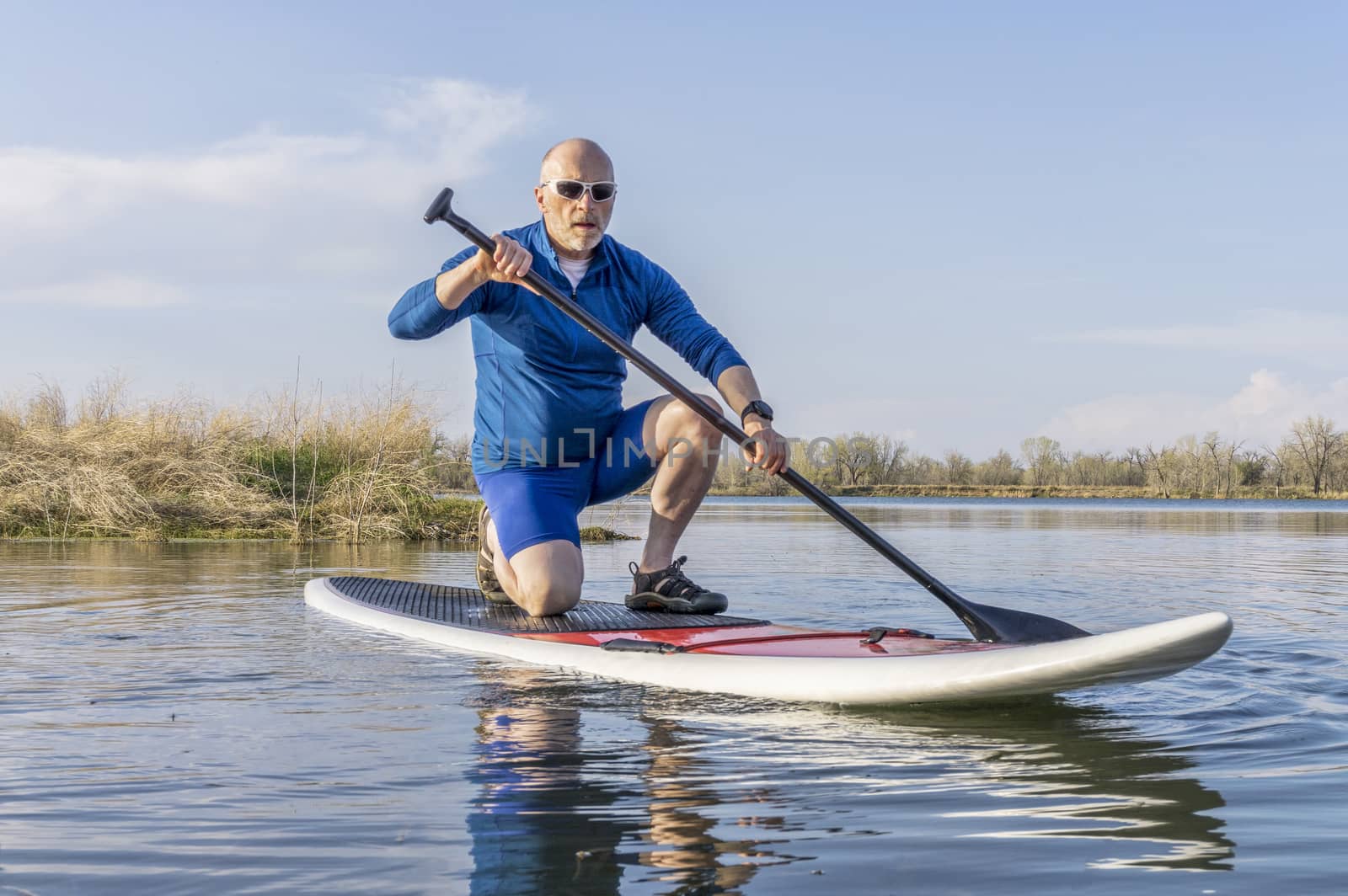 Senior male on stand up paddling (SUP) board. Early spring on calm lake in Colorado.