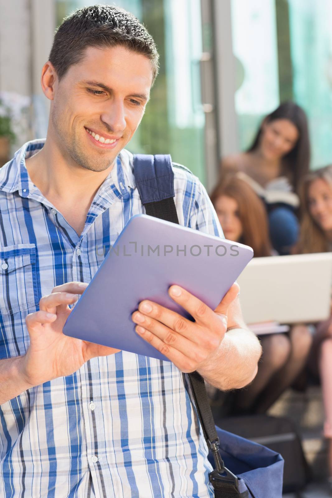 Happy student using his tablet pc on campus by Wavebreakmedia