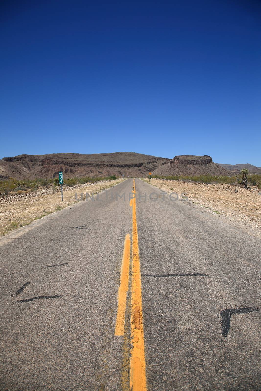 Desert road heads towards the mountains and buttes in Southwestern United States