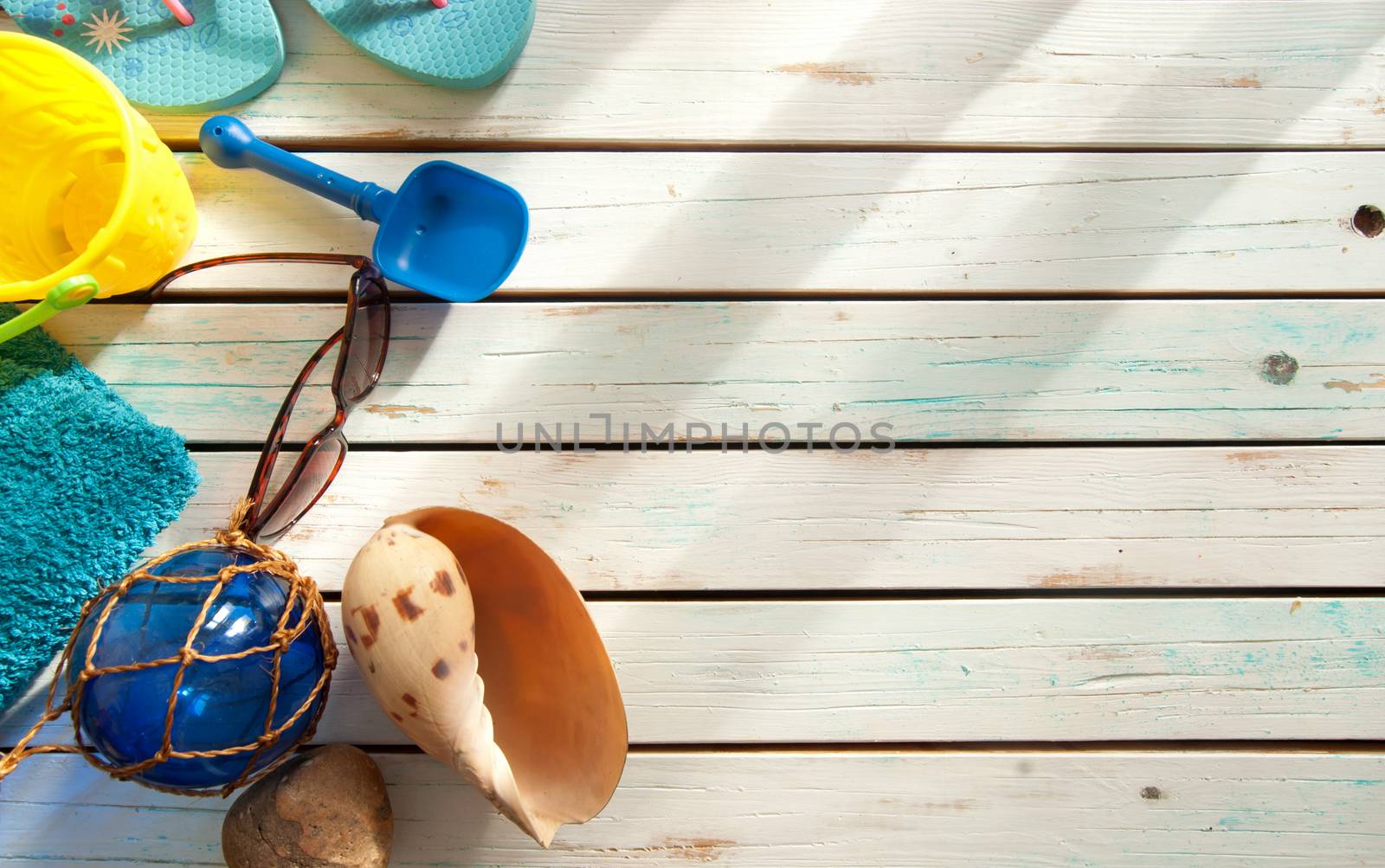 Summer vacation beach items including towel, sunglasses and bucket and spade over boards