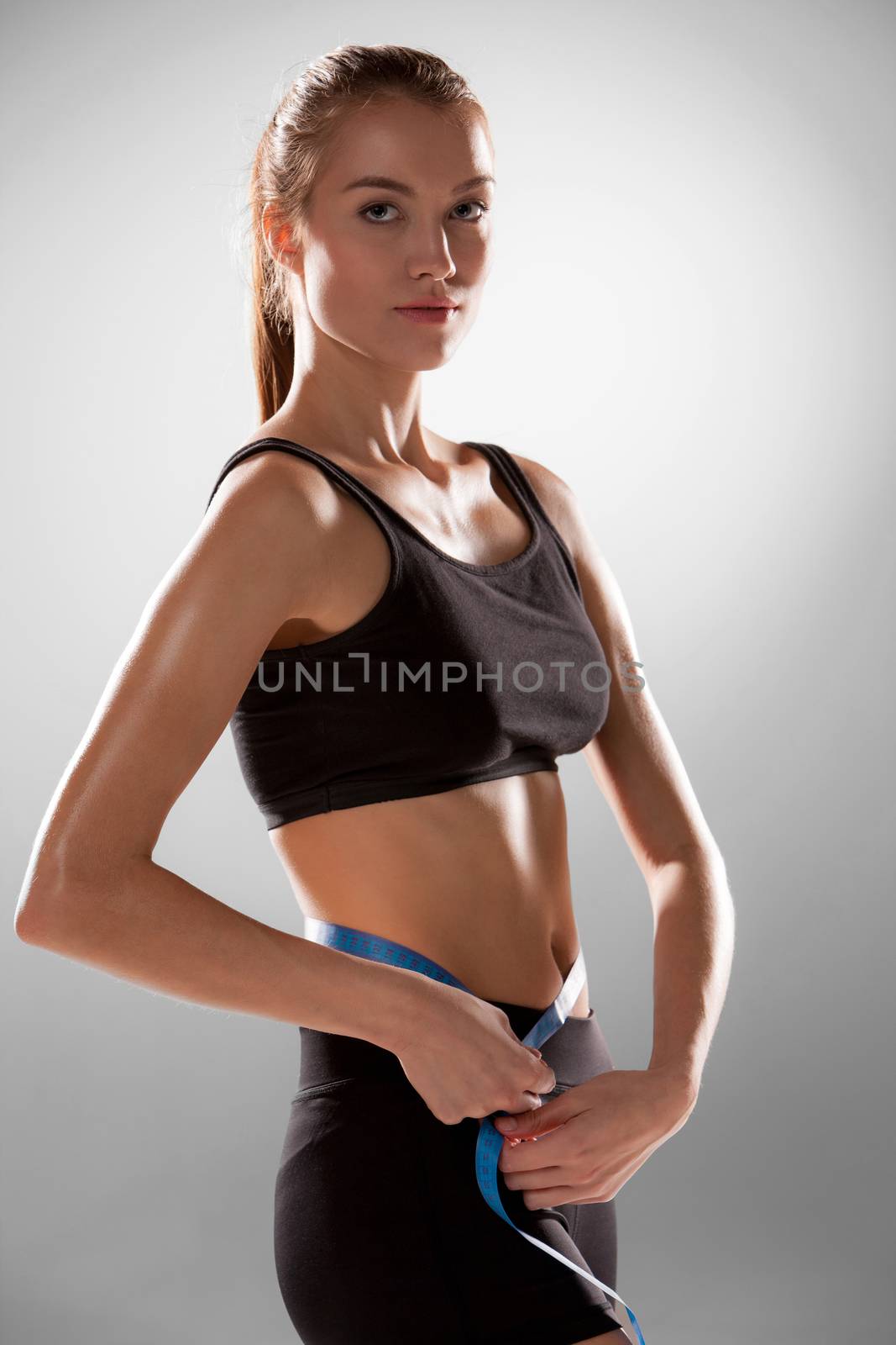 Sporty young woman with measuring tape on the gray background. Concept of healthy lifestyle.
