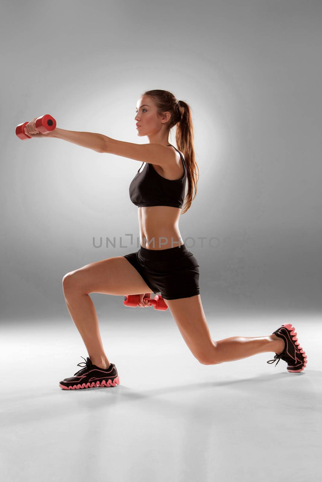 Sporty woman doing aerobic exercise with red dumbbells on grey background