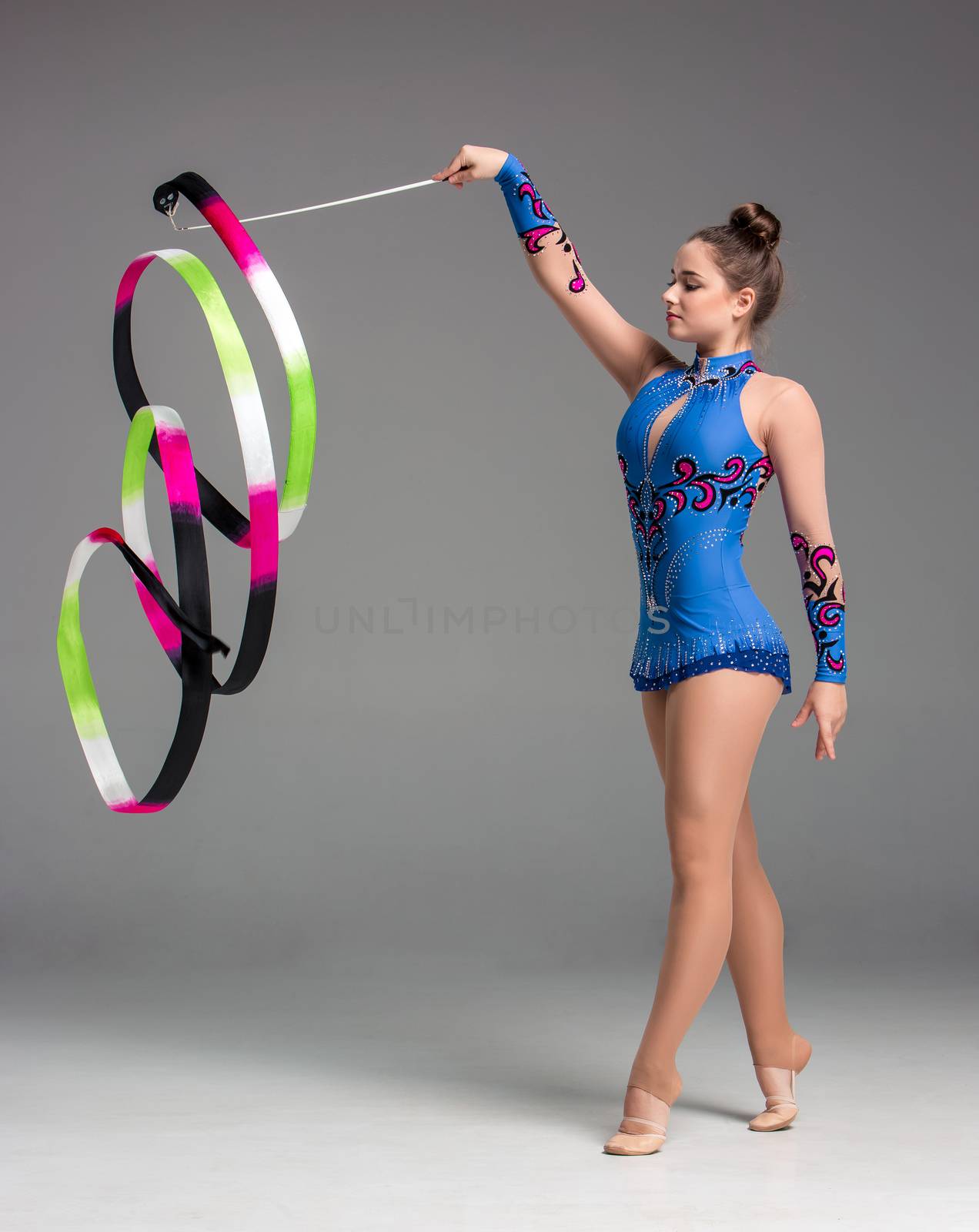 teenager doing gymnastics dance with colored ribbon on a gray background