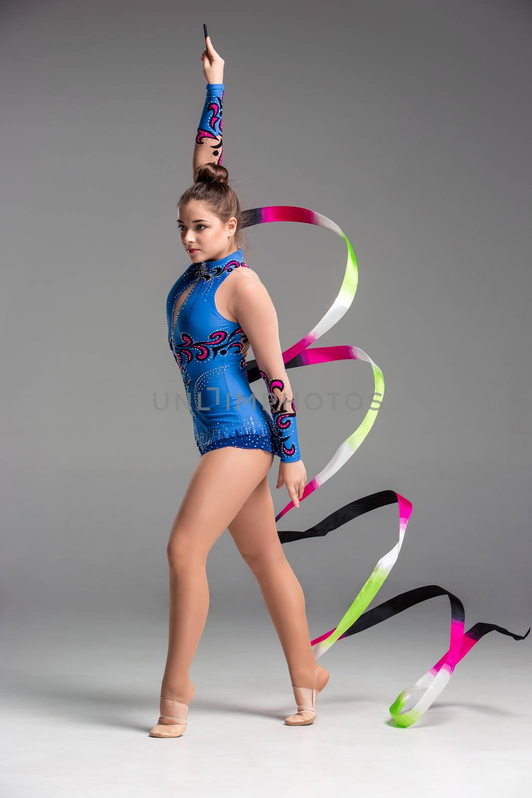teenager doing gymnastics dance with colored ribbon on a gray background