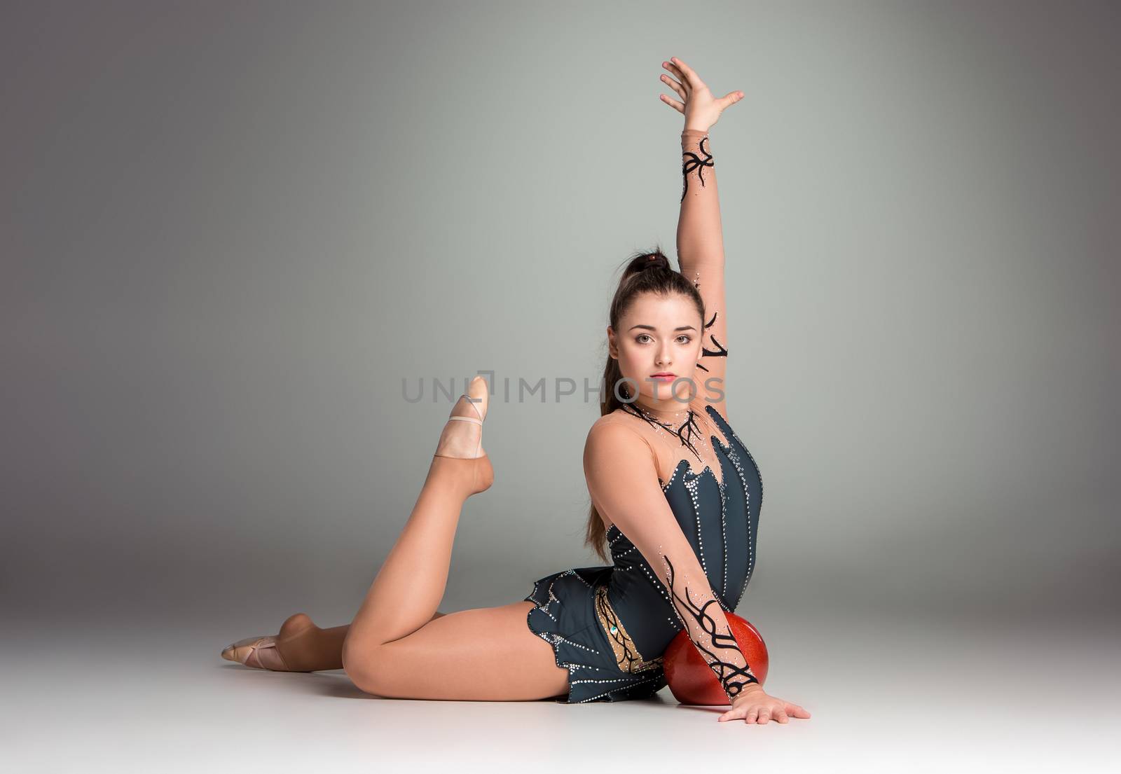 teenager doing gymnastics exercises with red gymnastic ball on a gray background