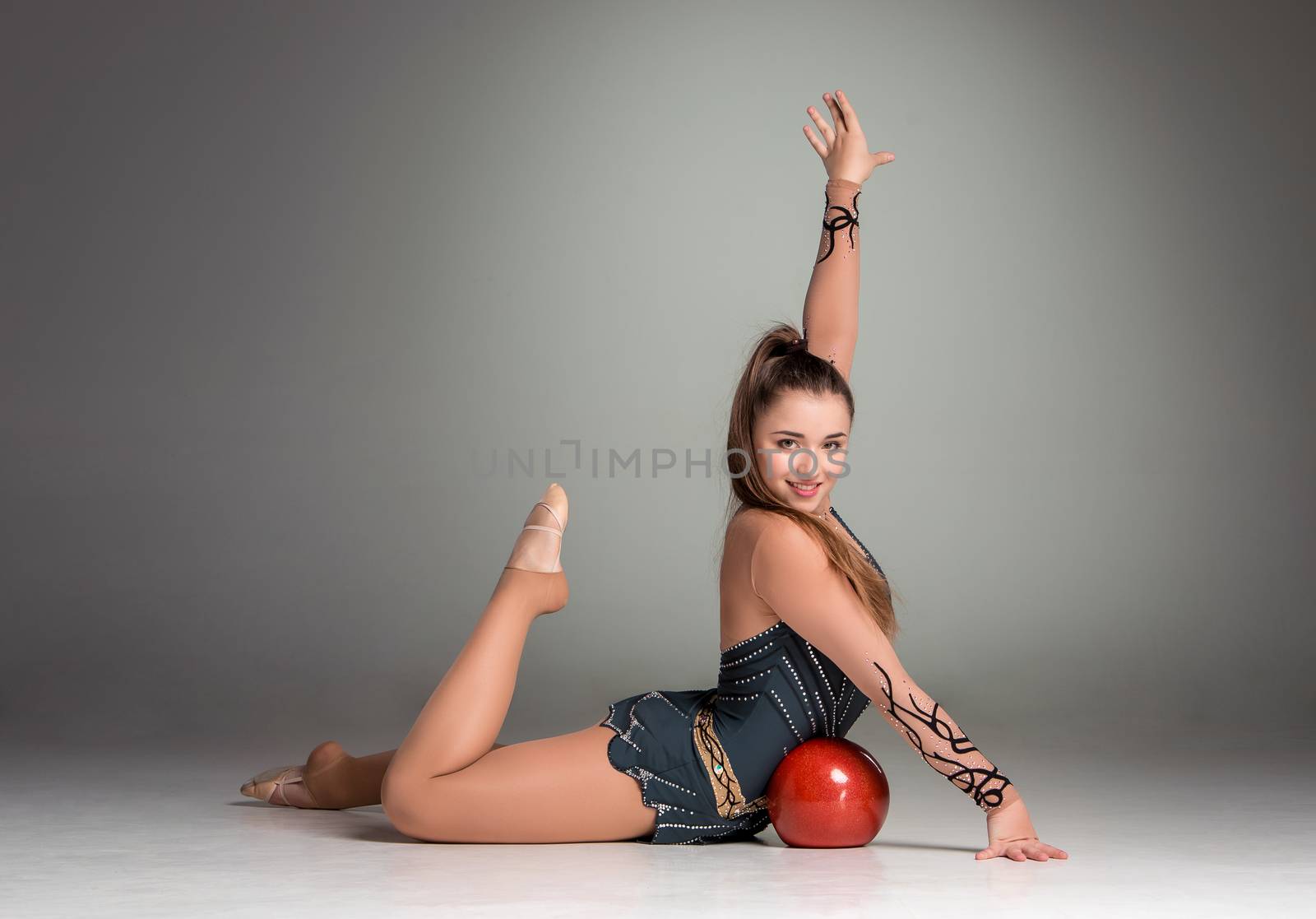 teenager doing gymnastics exercises with red gymnastic ball on a gray background