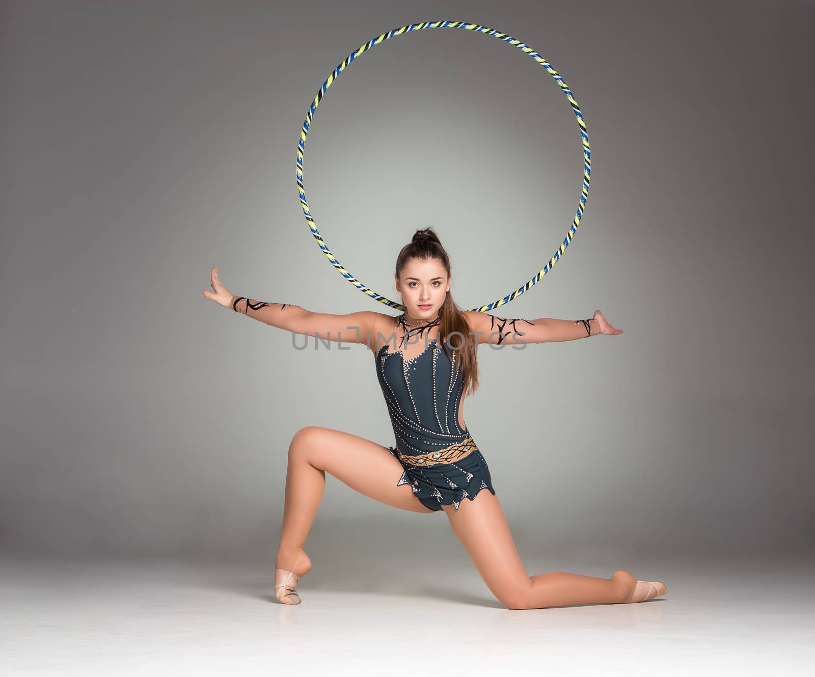 teenager doing gymnastics exercises with colorful hoop on a gray background