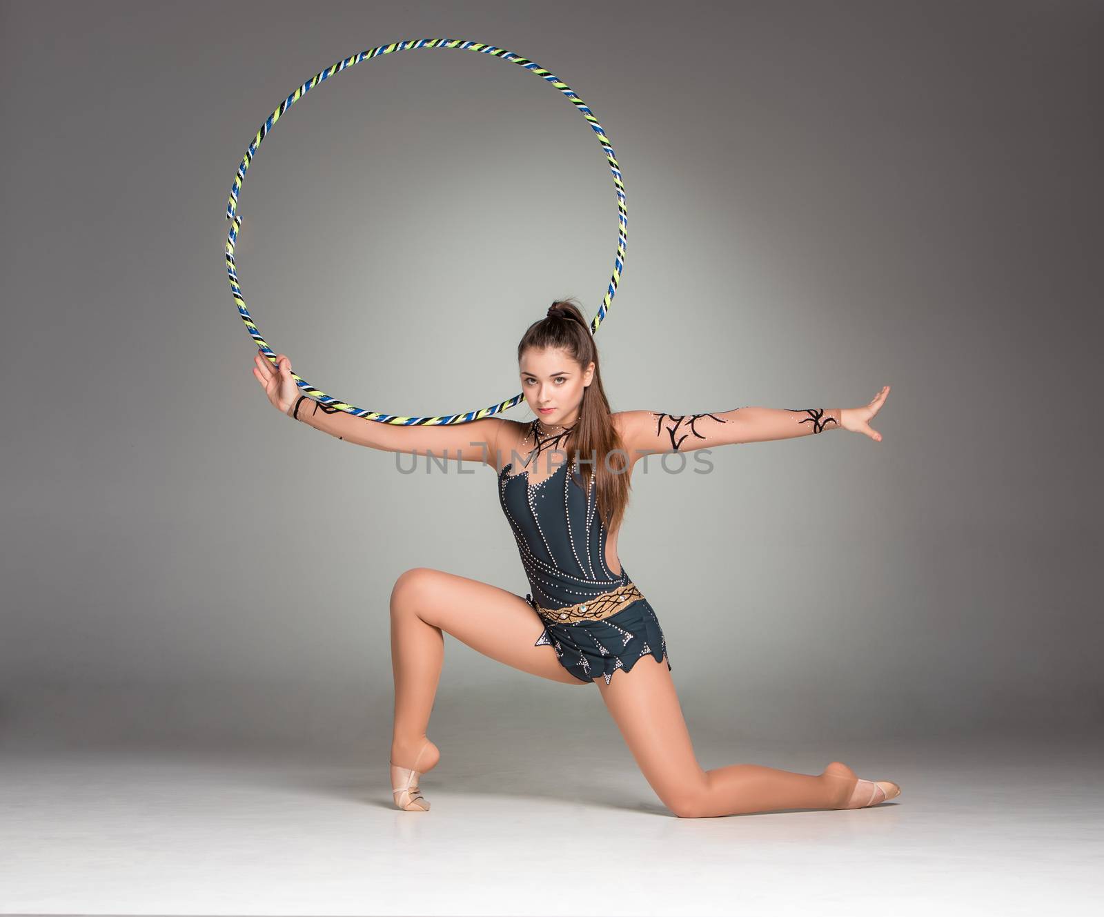 teenager doing gymnastics exercises with colorful hoop on a gray background