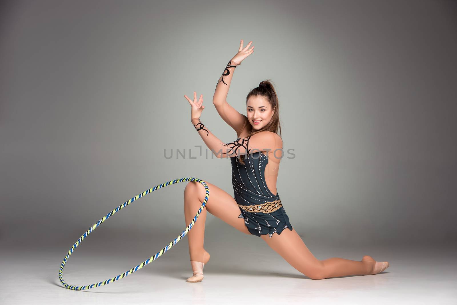 teenager doing gymnastics exercises with colorful hoop on a gray background