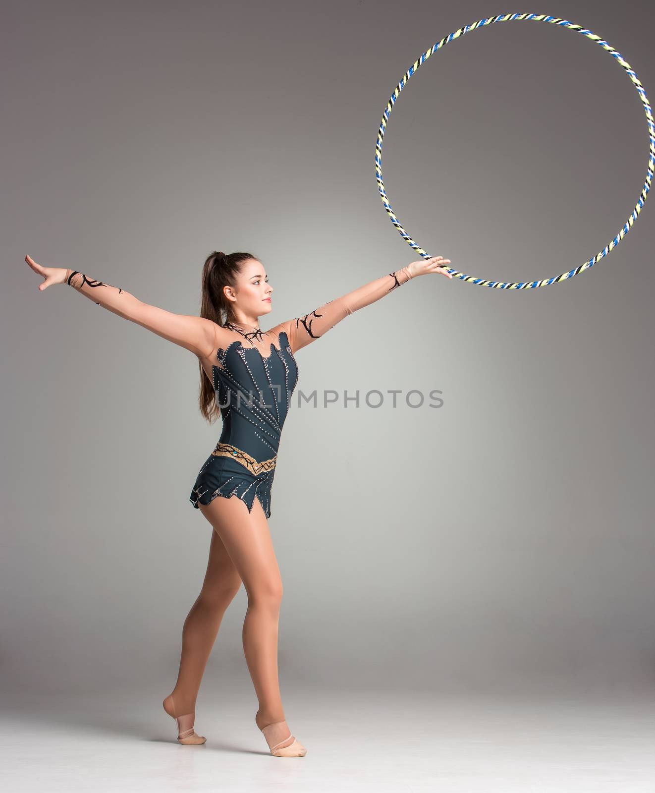 teenager doing gymnastics exercises with colorful hoop on a gray background