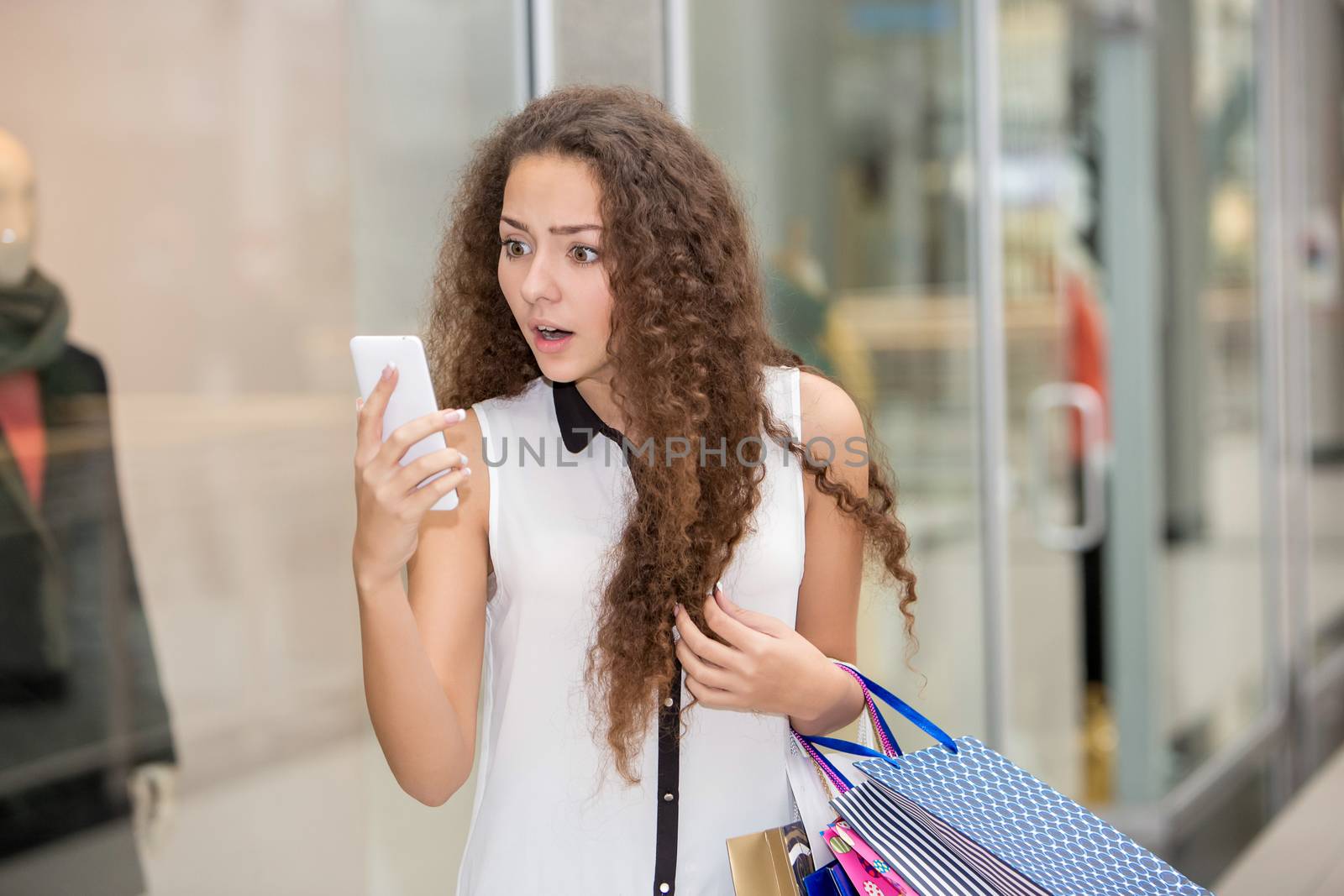 beautiful young woman goes shopping using a smartphone with a shopping bags in the mall