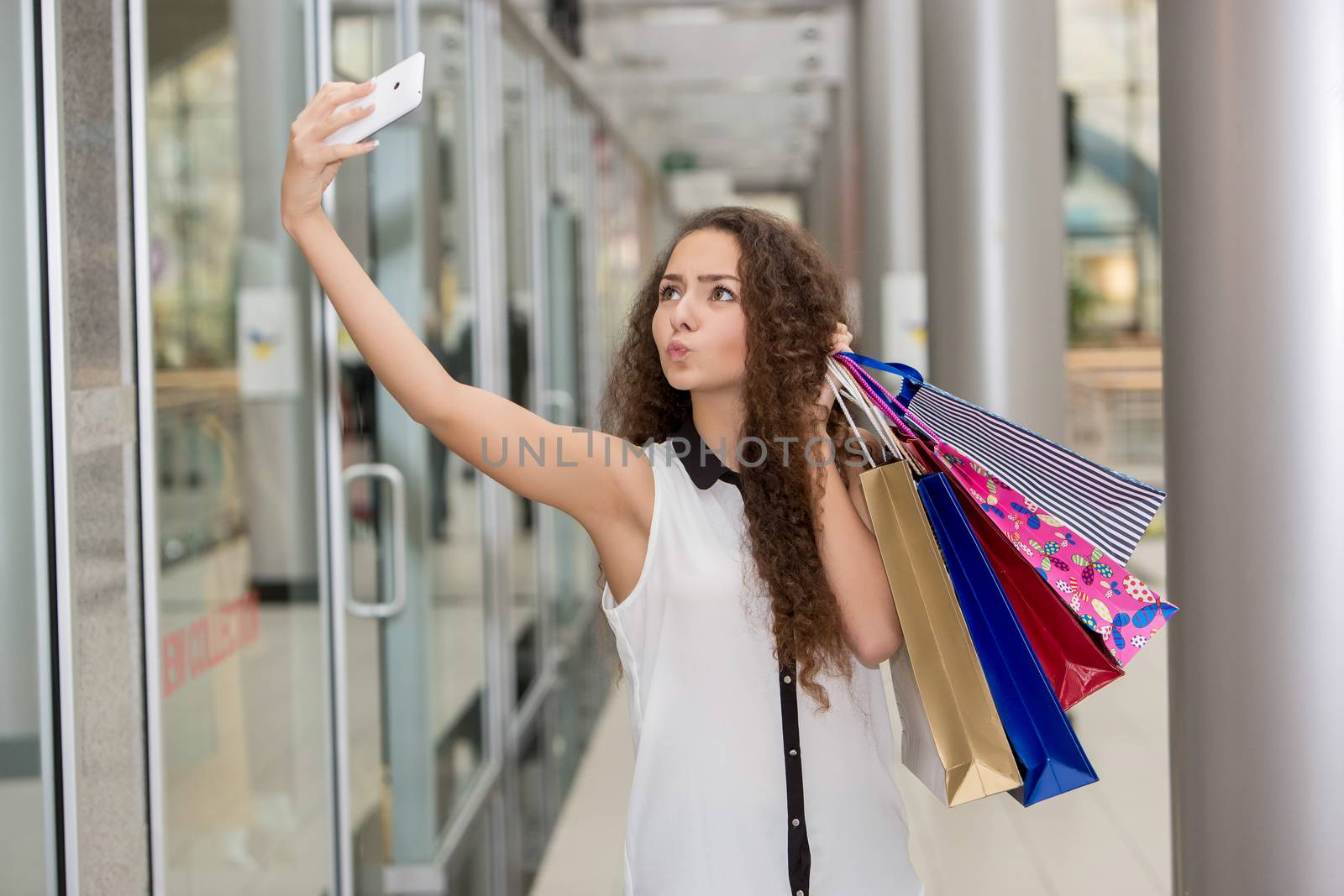 beautiful young woman goes shopping using a smartphone with a shopping bags in the mall