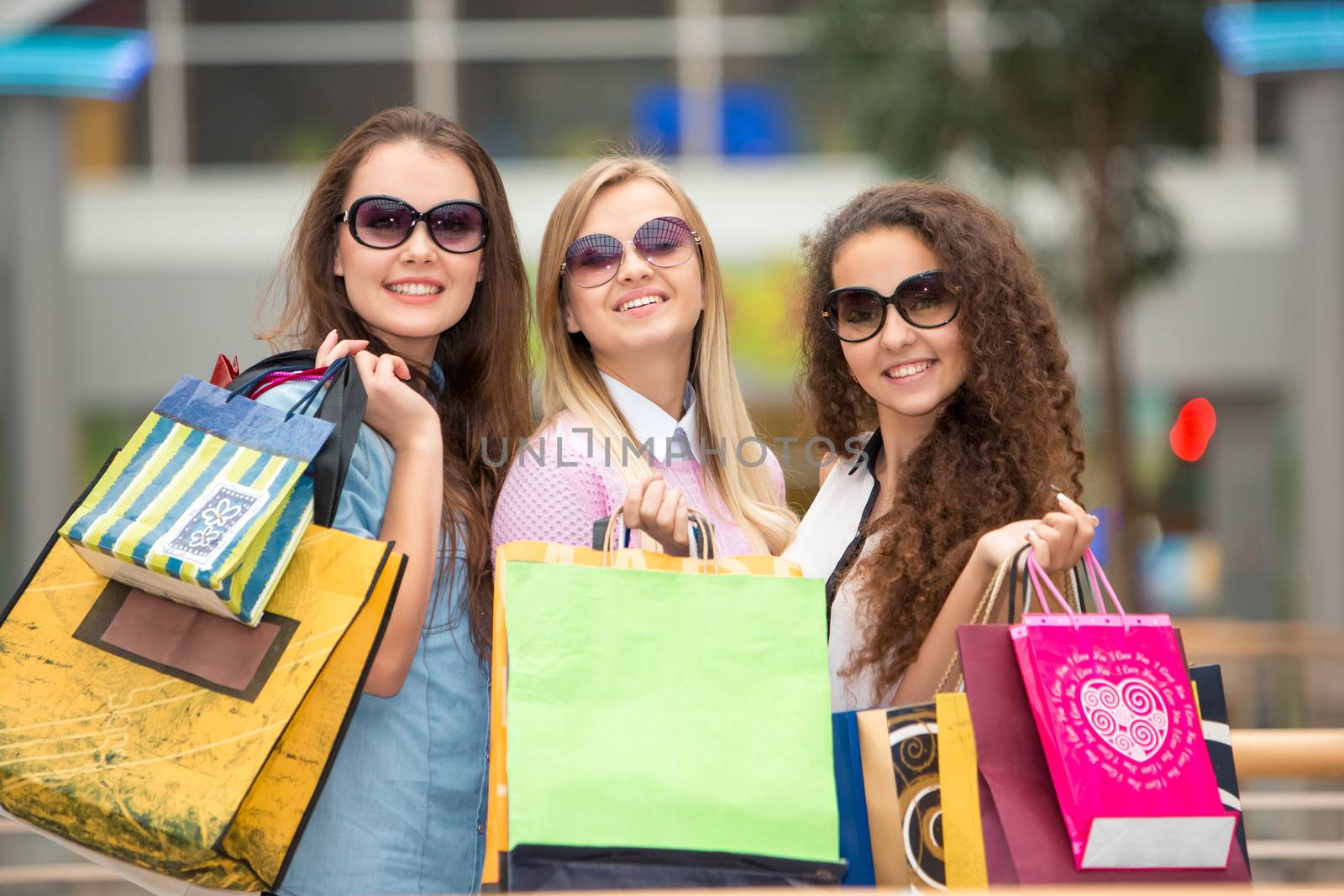 shopping, sale, happy people and tourism concept - three beautiful girls in sunglasses with shopping bags in mall
