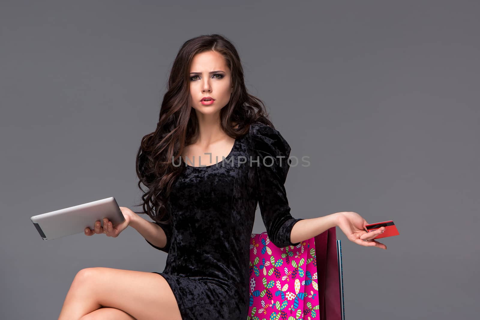 Beautiful young girl paying by credit card for shopping with a laptop and packages against gray background