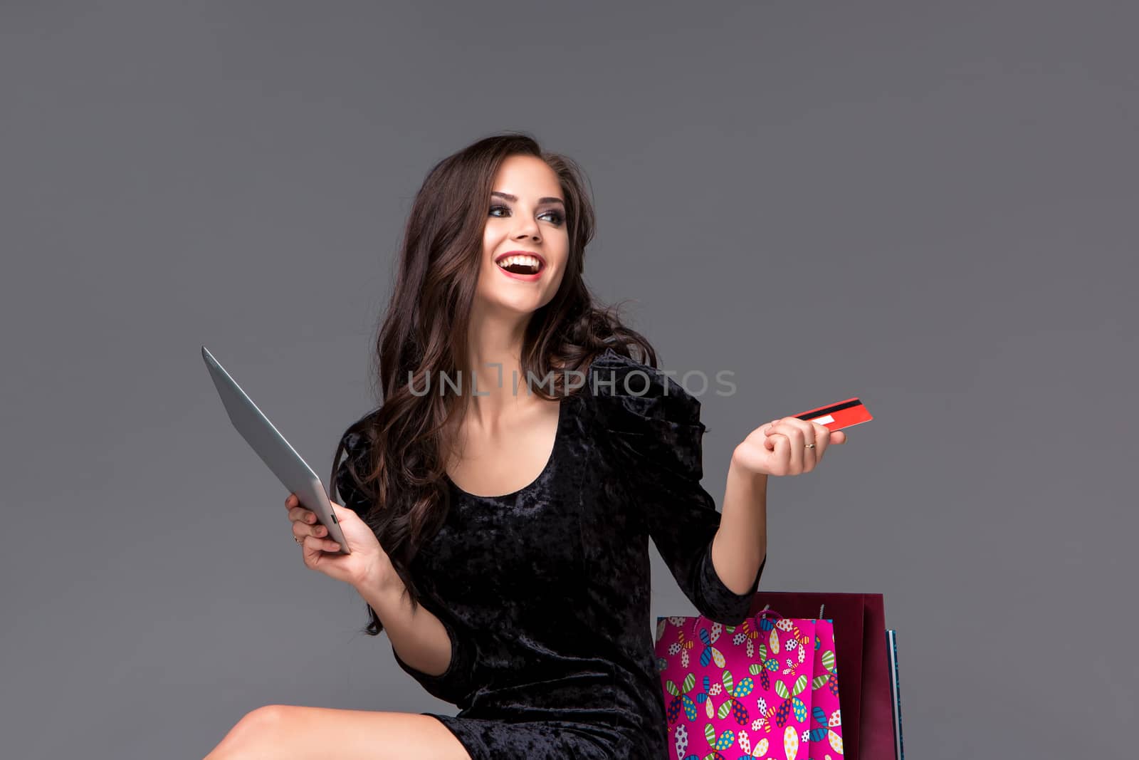 Beautiful young girl paying by credit card for shopping with a laptop and packages against gray background