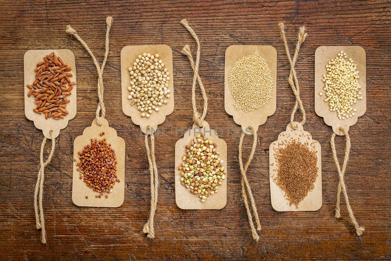 abstract of healthy, gluten free grains (quinoa, sorghum, brown rice, teff, buckwheat, amaranth, millet) - top view of paper price tags against rustic wood