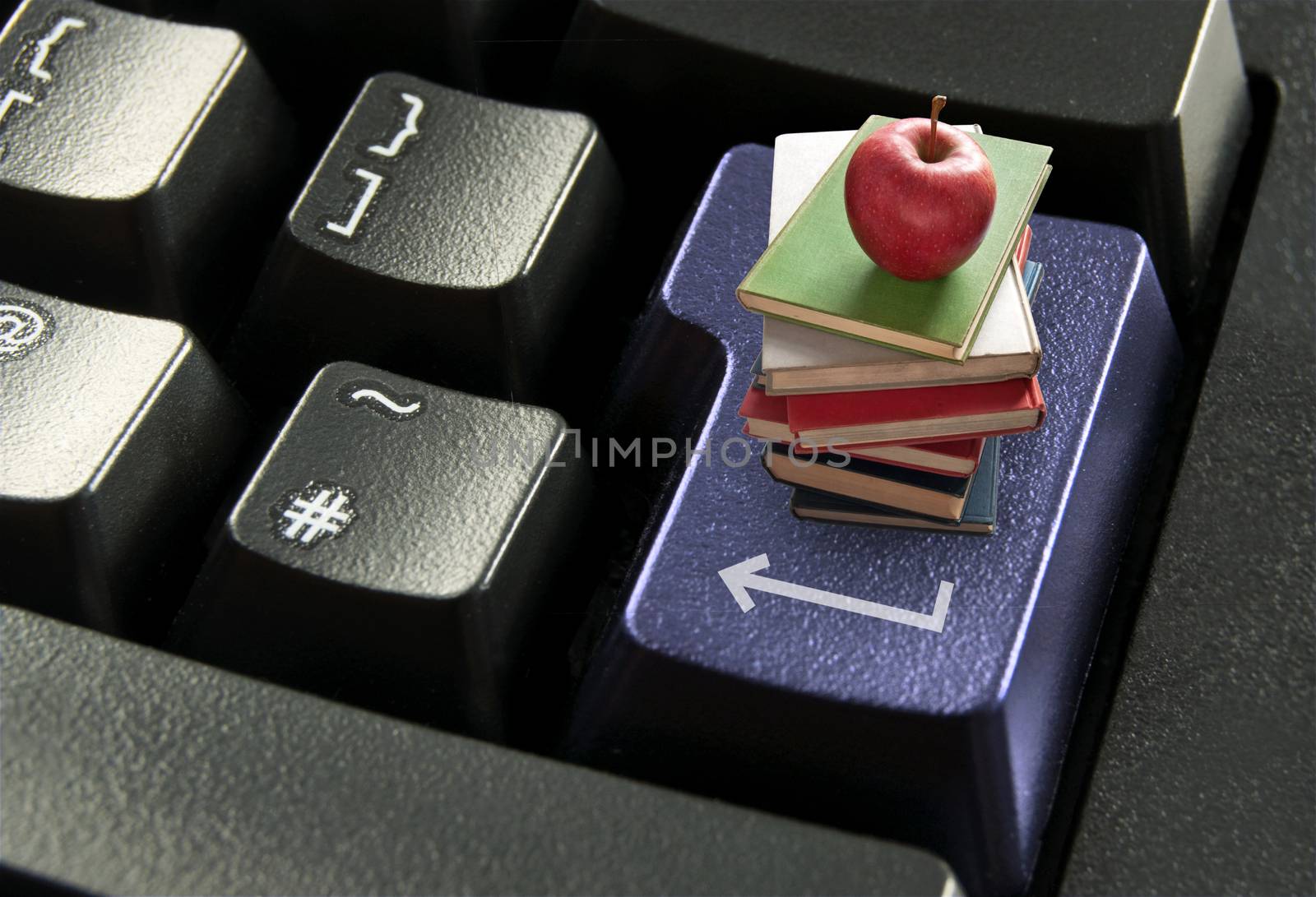 Stack of books with red apple on top of a computer enter key