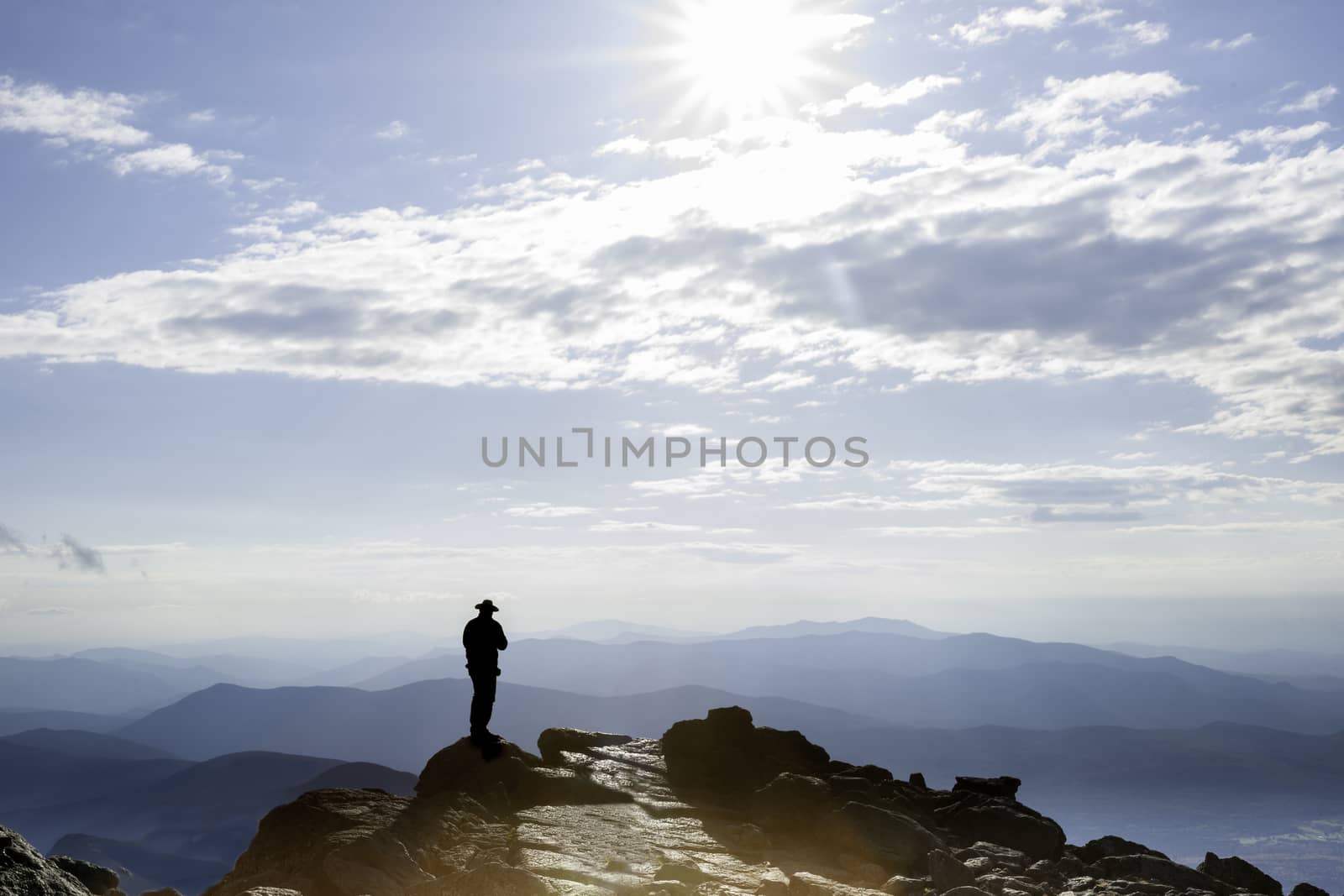 Sun filtered by clouds hits the rocky top on Mount Washington and the silhouette of man on top, New Hampshire, USA